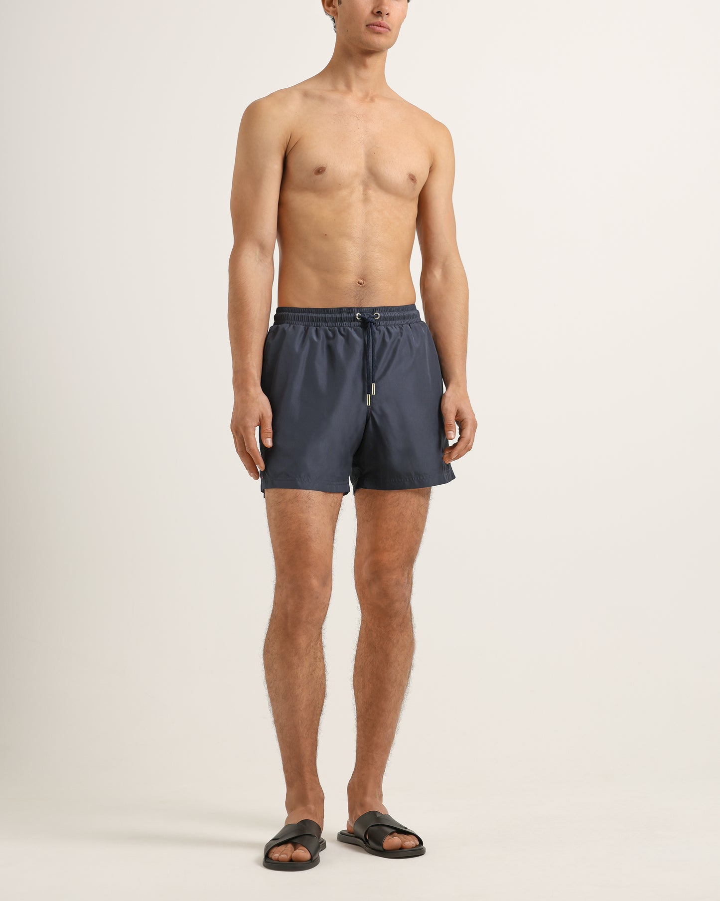 Man wearing dark gray swim shorts on a plain background