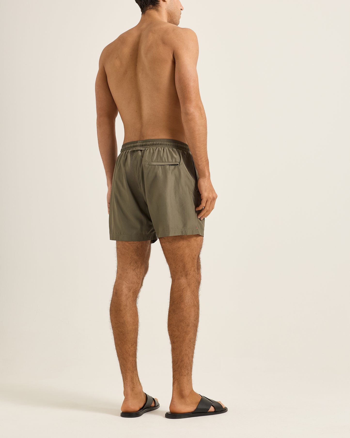Man wearing olive green swim shorts on a plain background