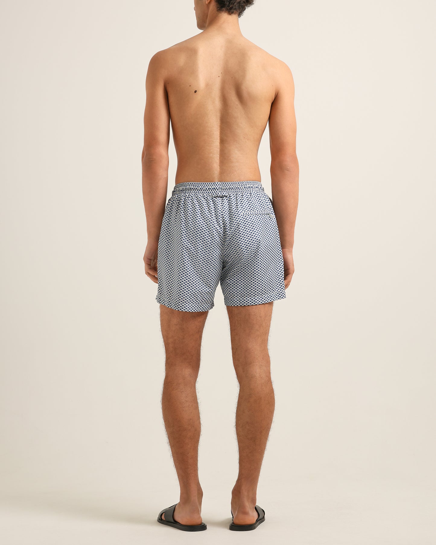 Person wearing blue checkered swim shorts on a beige background