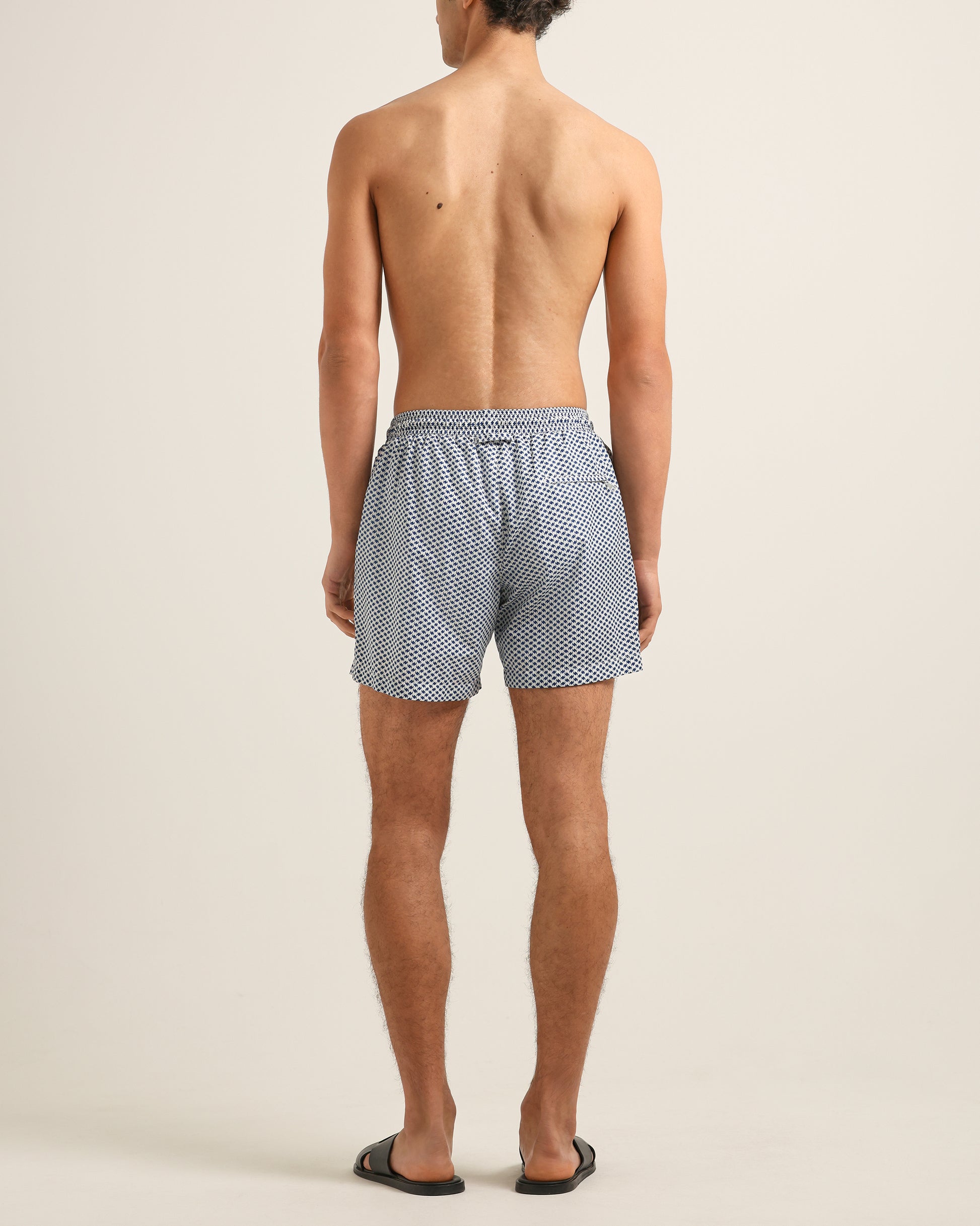 Person wearing blue checkered swim shorts on a beige background