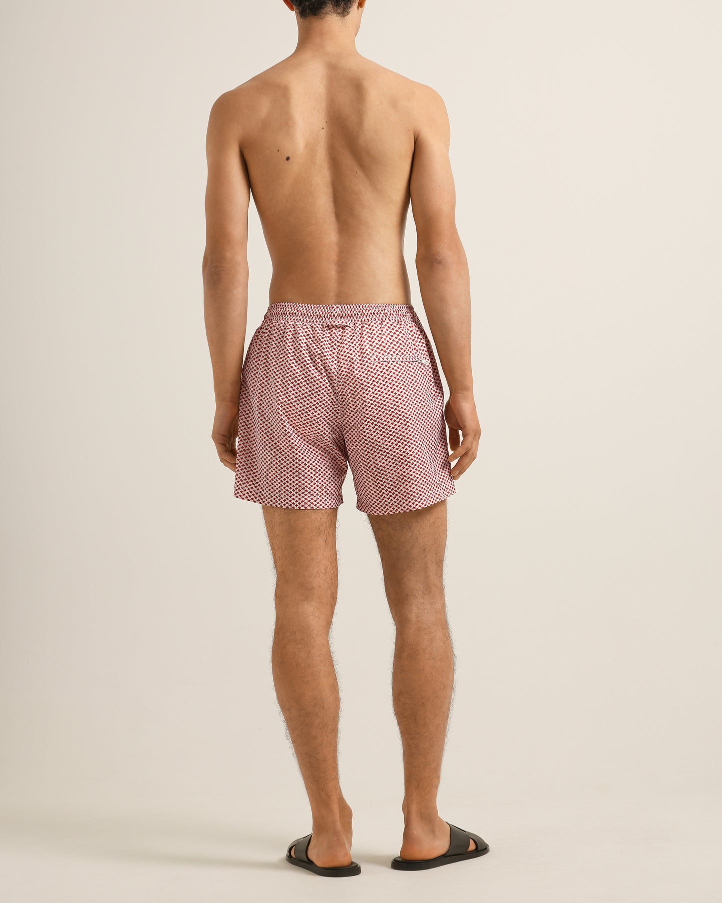 Person wearing red patterned swim shorts on a beige background