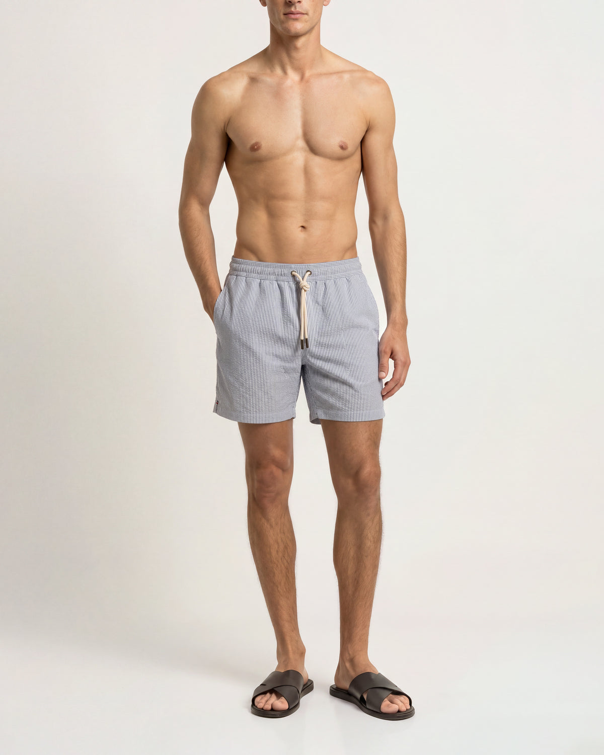 A man modeling light gray drawstring shorts and dark brown slide sandals against a plain white studio background.