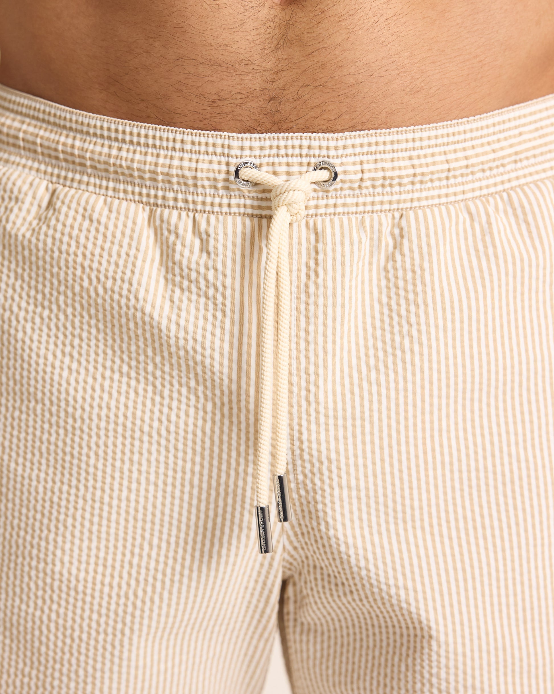 Close-up of beige shorts with a drawstring on a person.