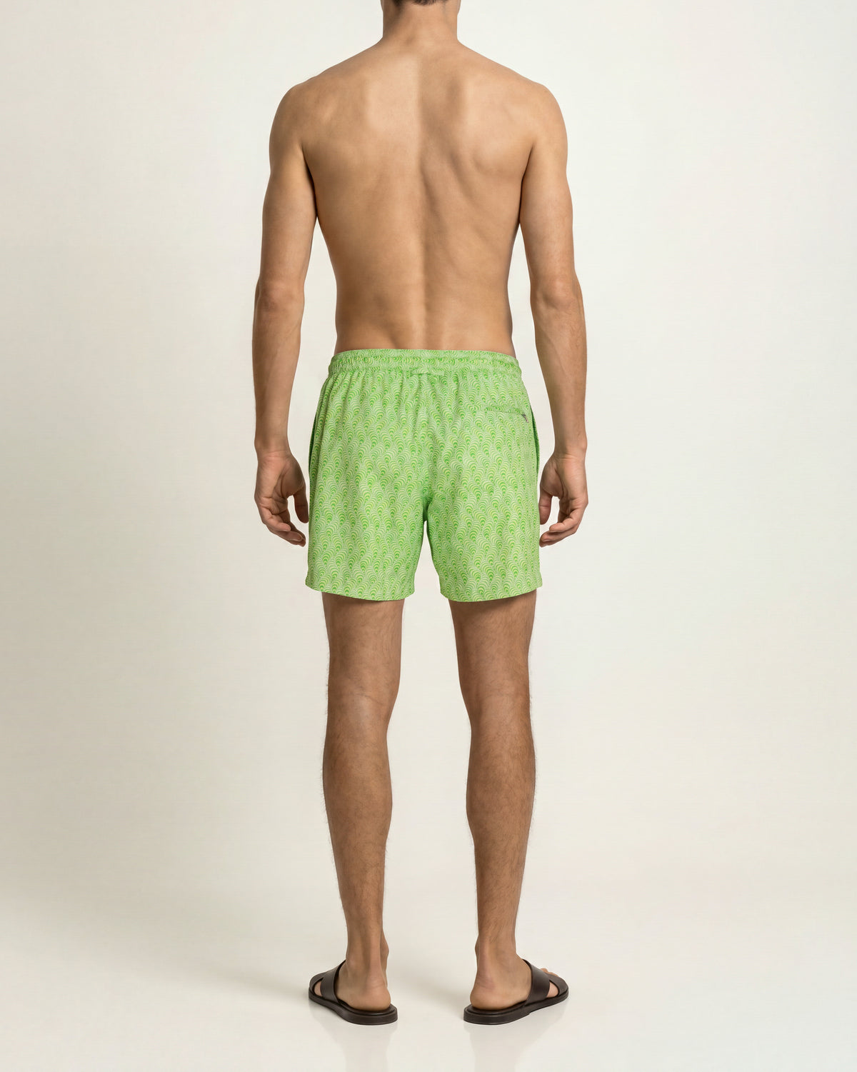Man wearing bright green patterned swim short on a plain background