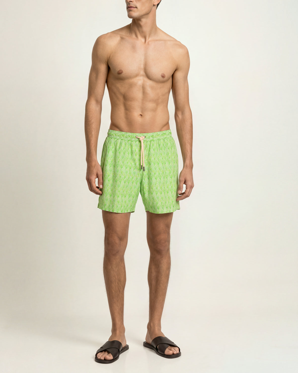 Man wearing bright green patterned swim short on a plain background