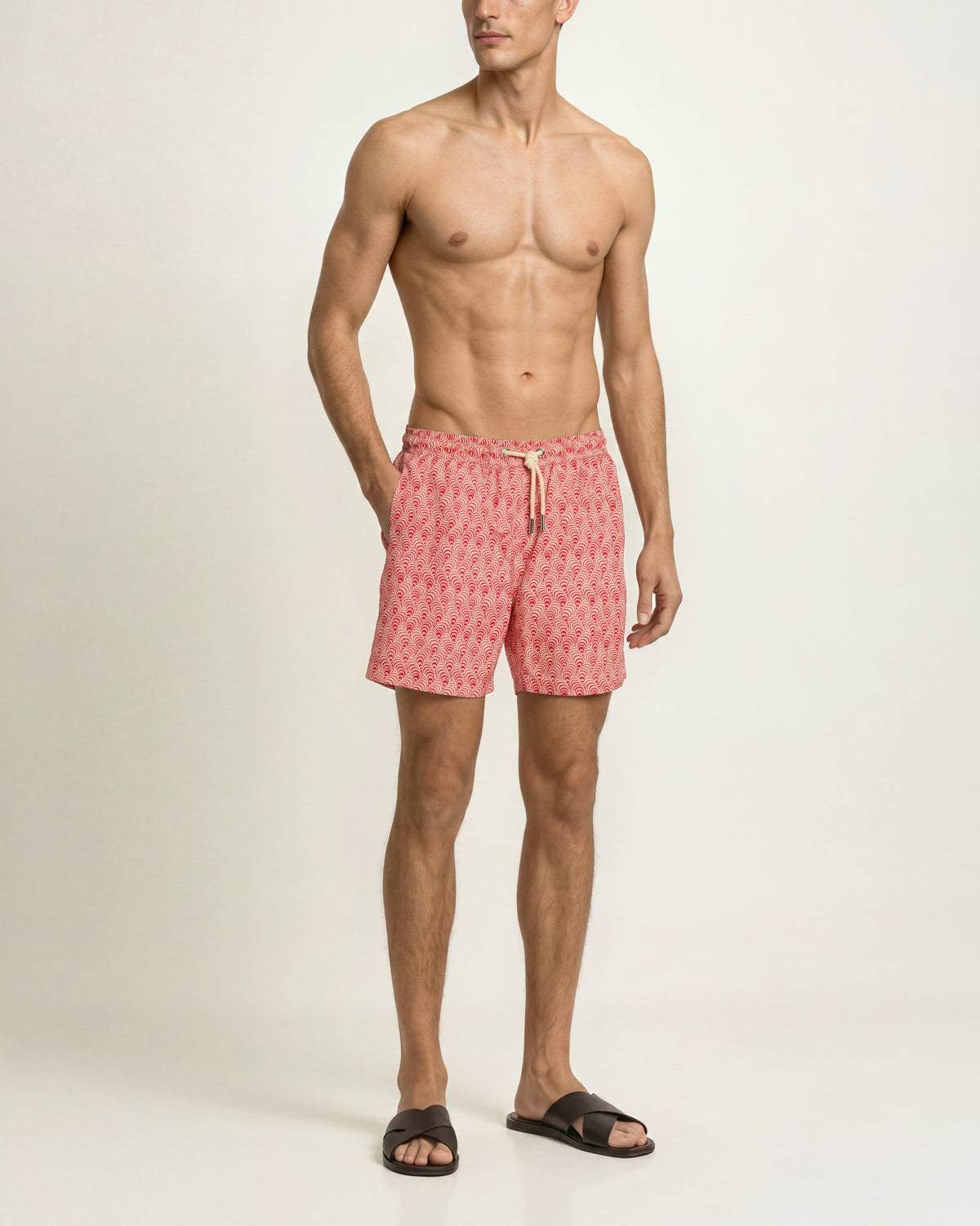 Man wearing red patterned swim shorts with brown sandals on a plain background