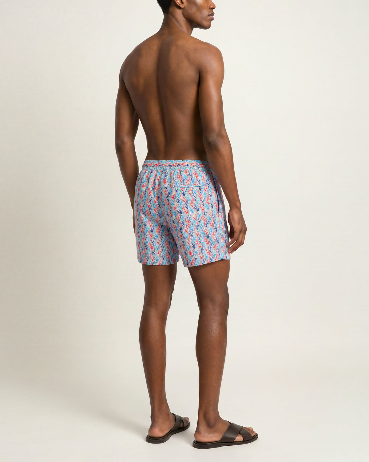 Man wearing blue and pink patterned swim shorts with brown sandals on a plain background