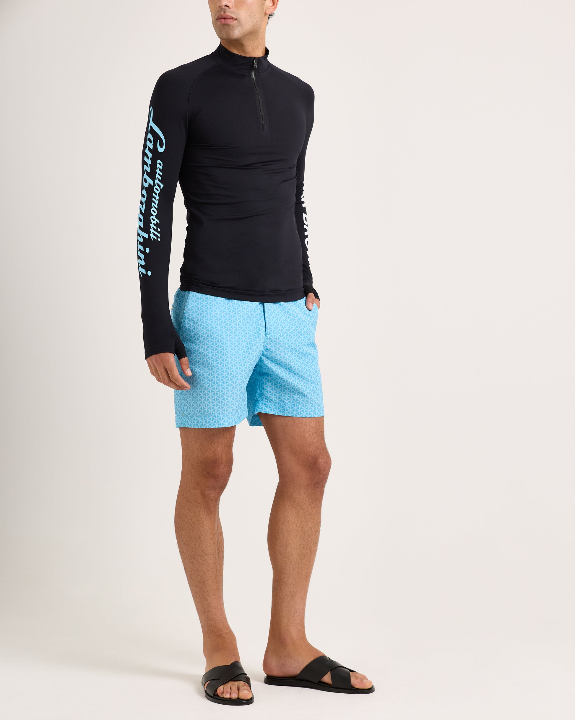 Person wearing a black long-sleeve shirt with white text and light blue swim shorts on a white background