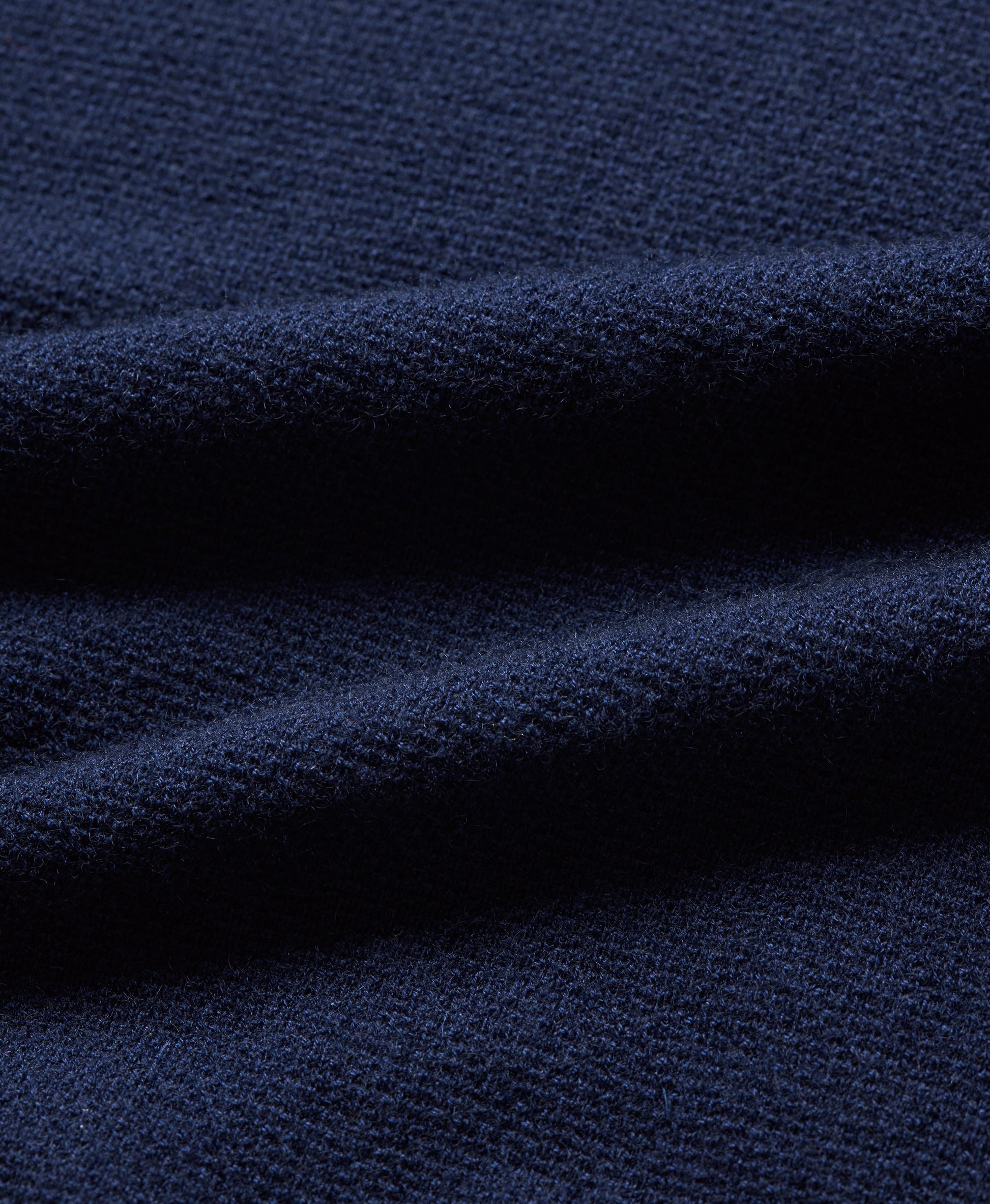 A close-up of dark navy blue knit fabric with soft folds showing the textured weave.