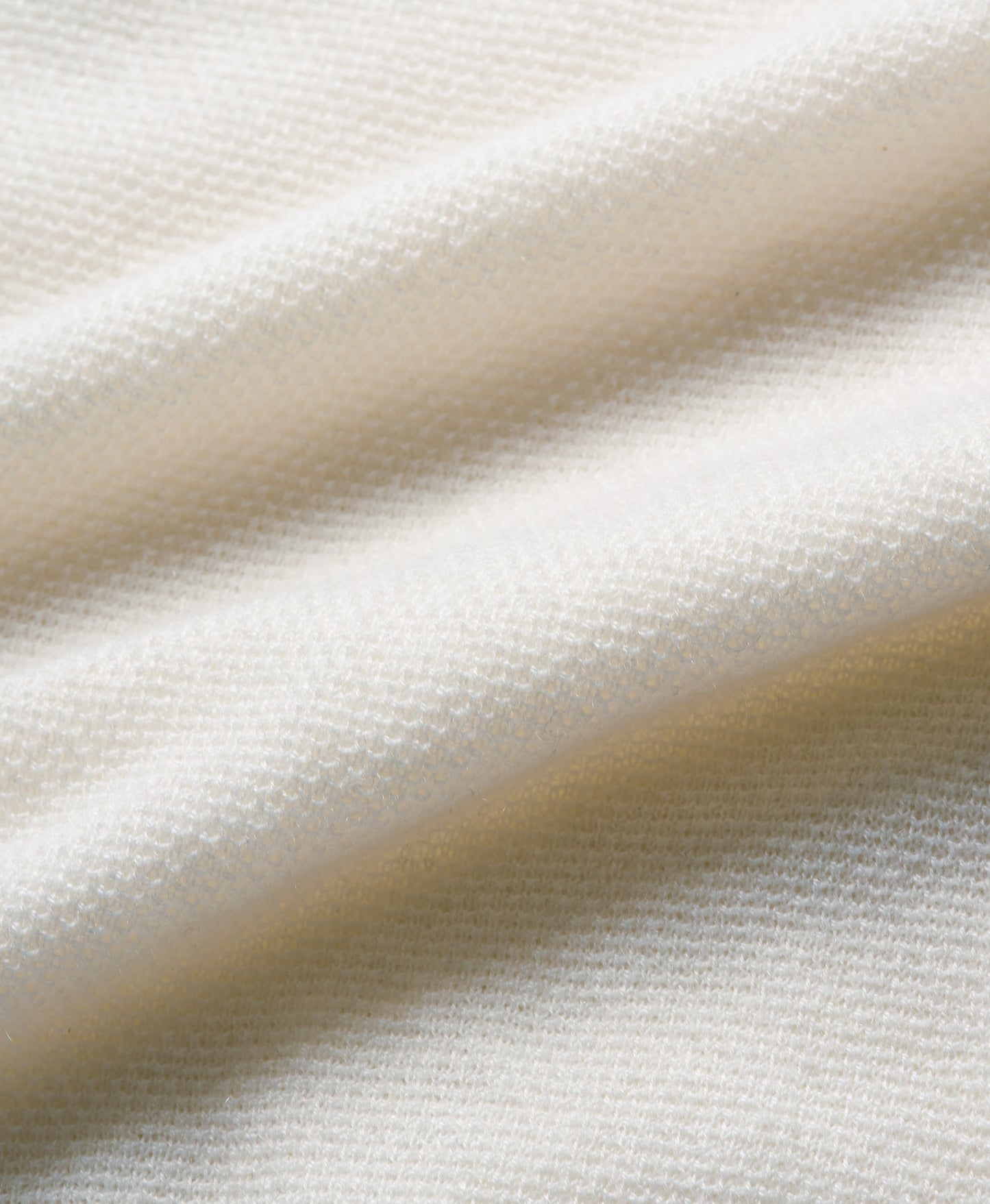 A close-up of draped off-white fabric with a fine textured weave, showing soft folds and shadows.