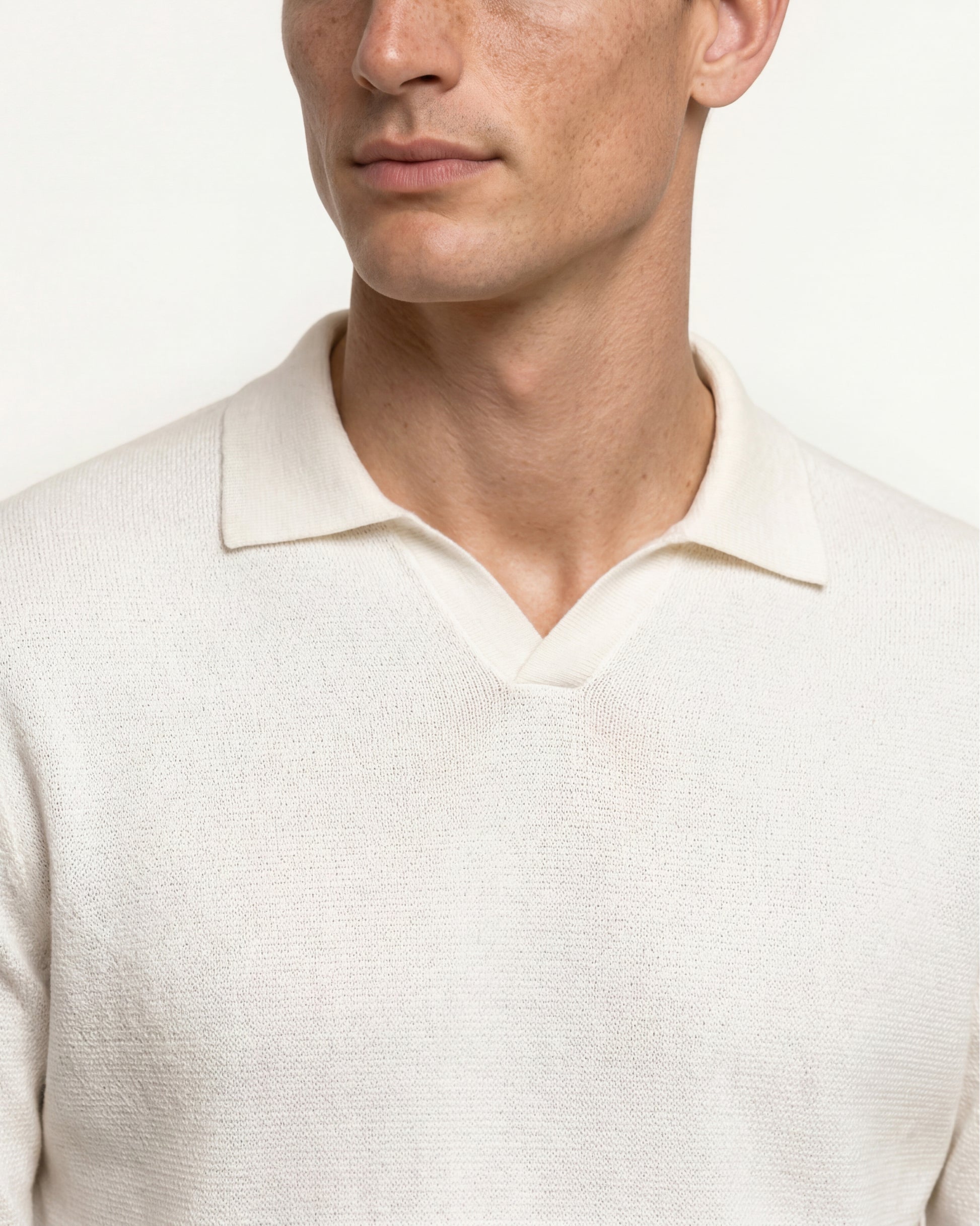 Close-up of a man wearing a cream-colored knit polo sweater against a plain light background.