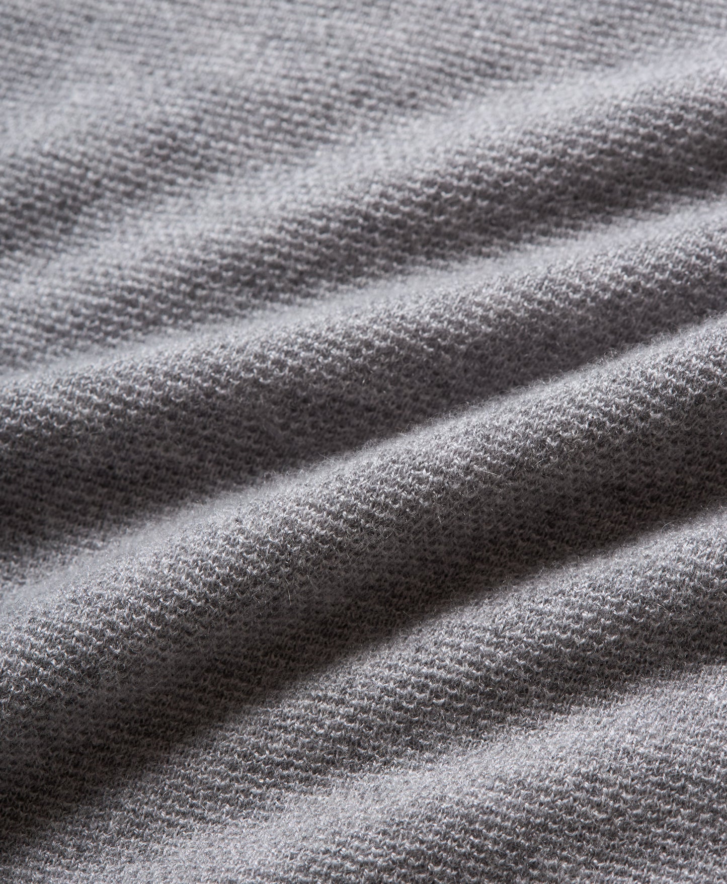 Close-up of a gray knit fabric with a fine textured pattern and soft draped folds.