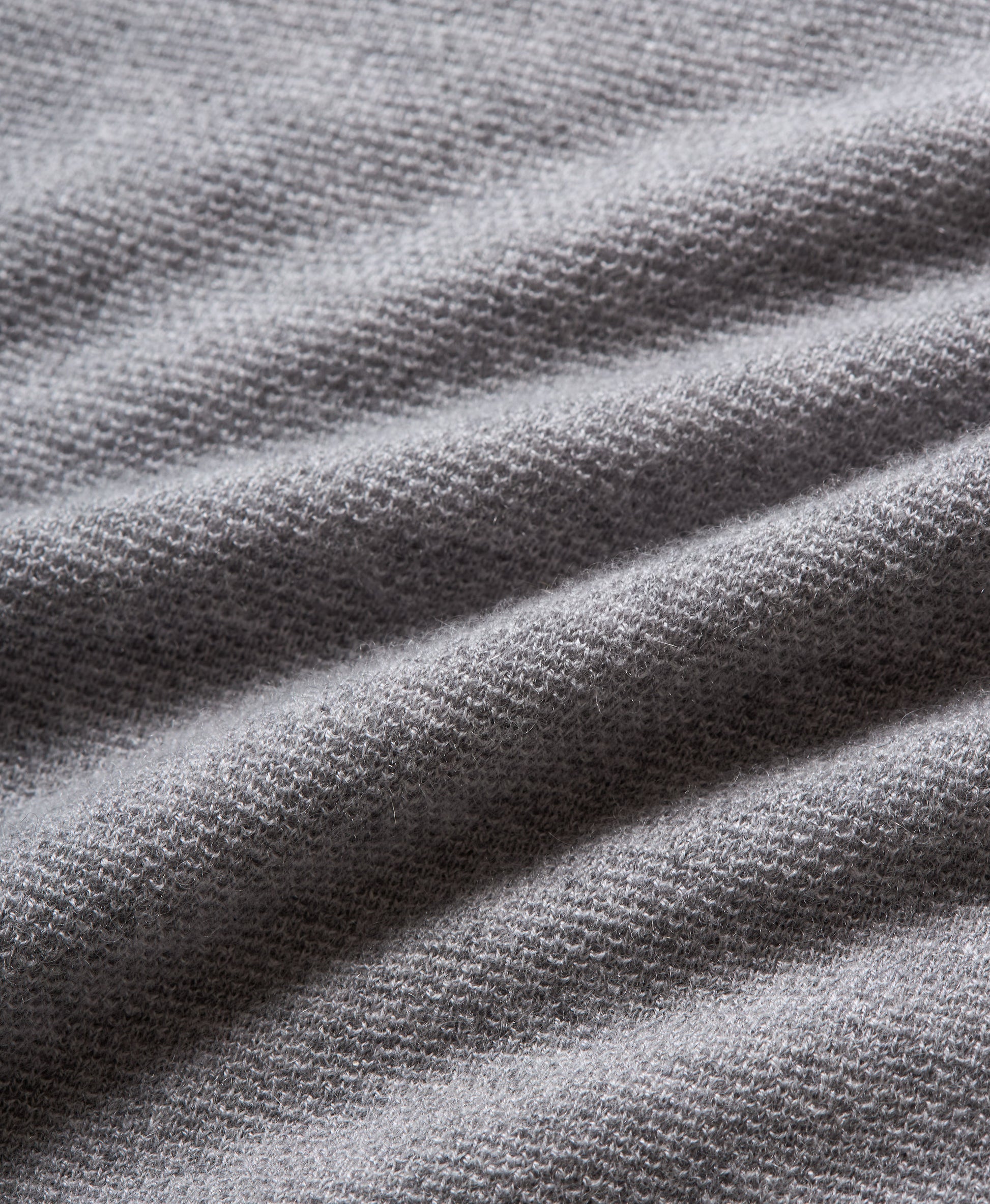 Close-up of a gray knit fabric with a fine textured pattern and soft draped folds.