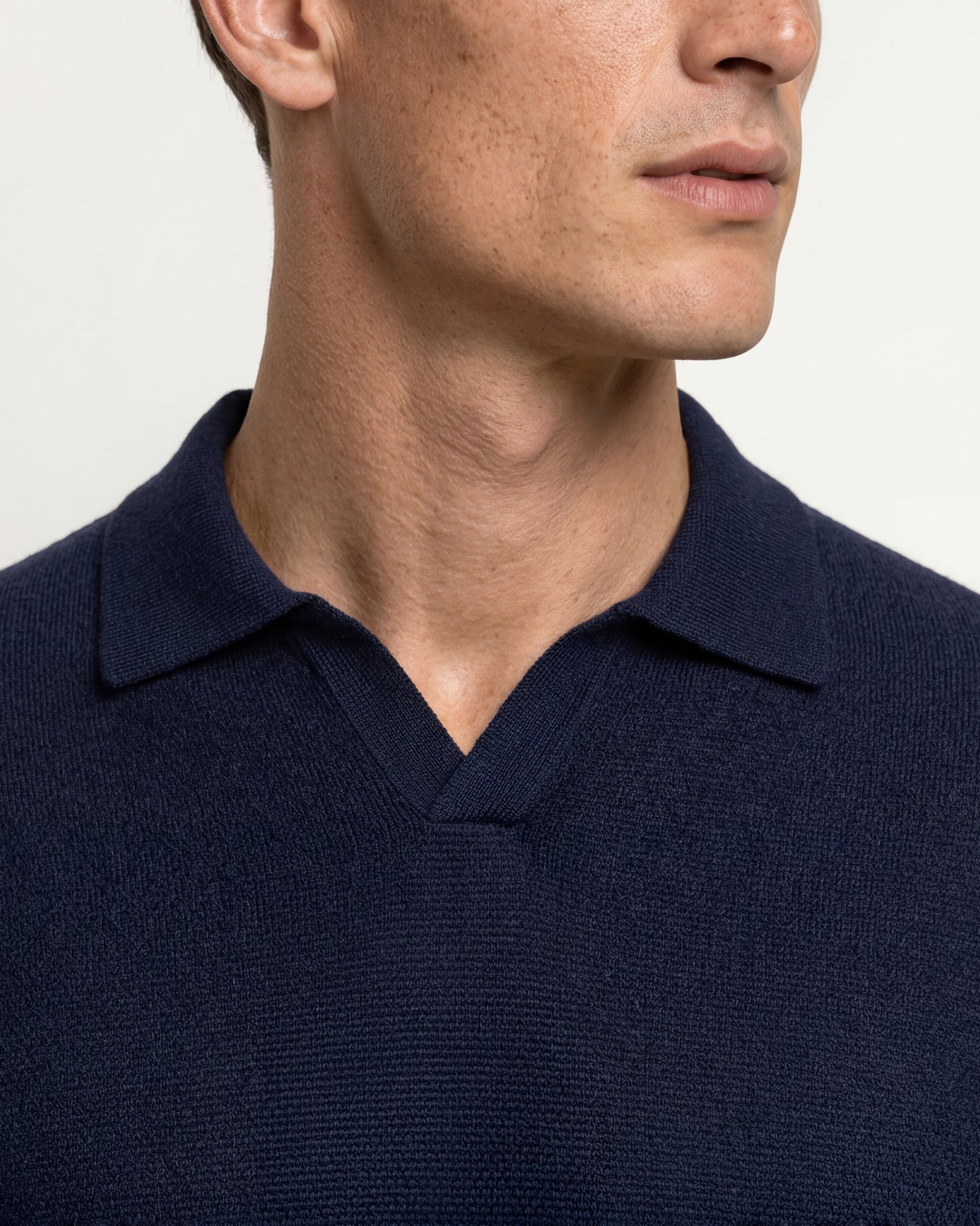Close-up of a man wearing a dark navy blue knit polo shirt, showing the collar and textured fabric against a plain light background.