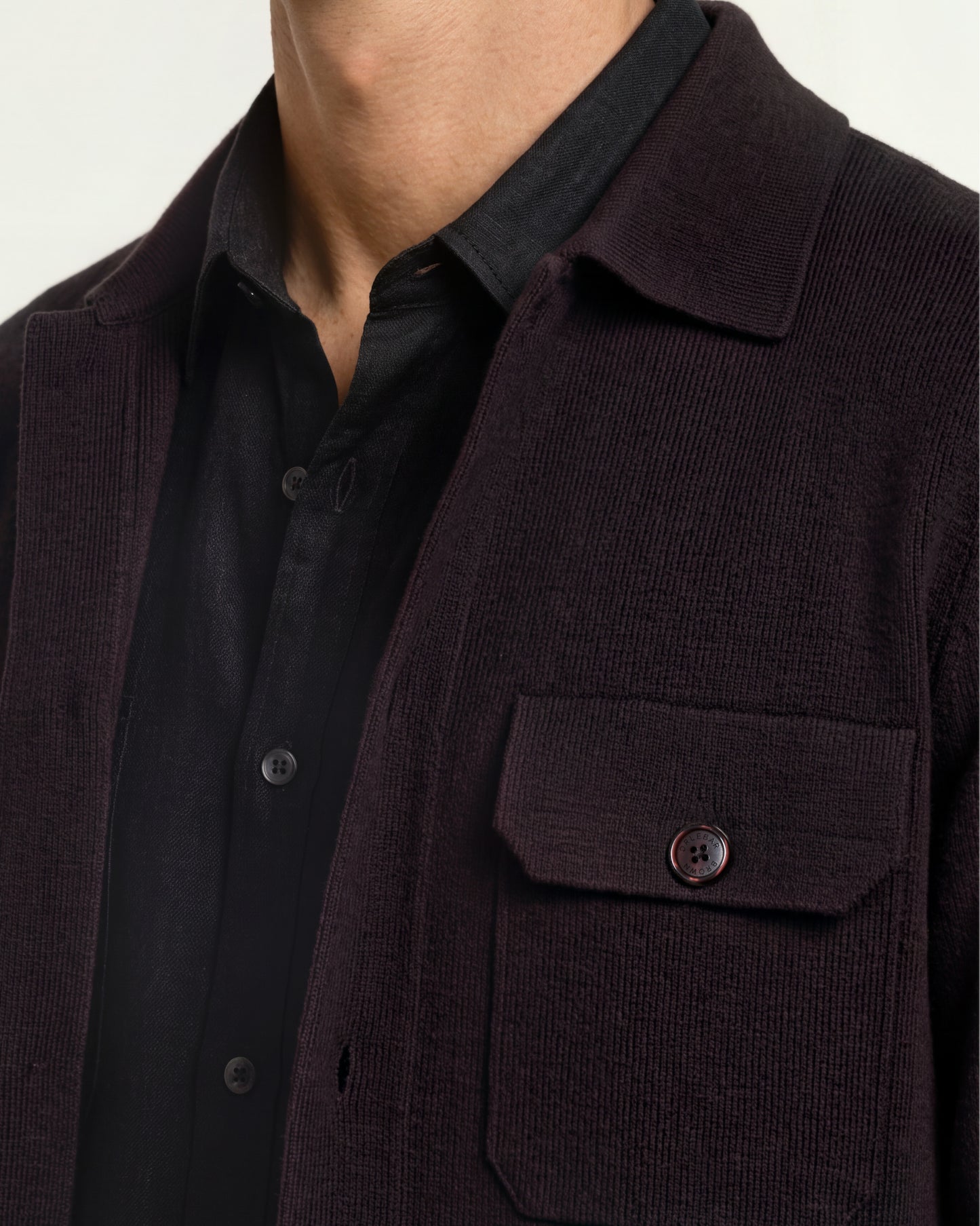 Close-up of a person wearing a dark brown corduroy jacket over a black button-up shirt, showing the collar, chest pocket, and corduroy texture.