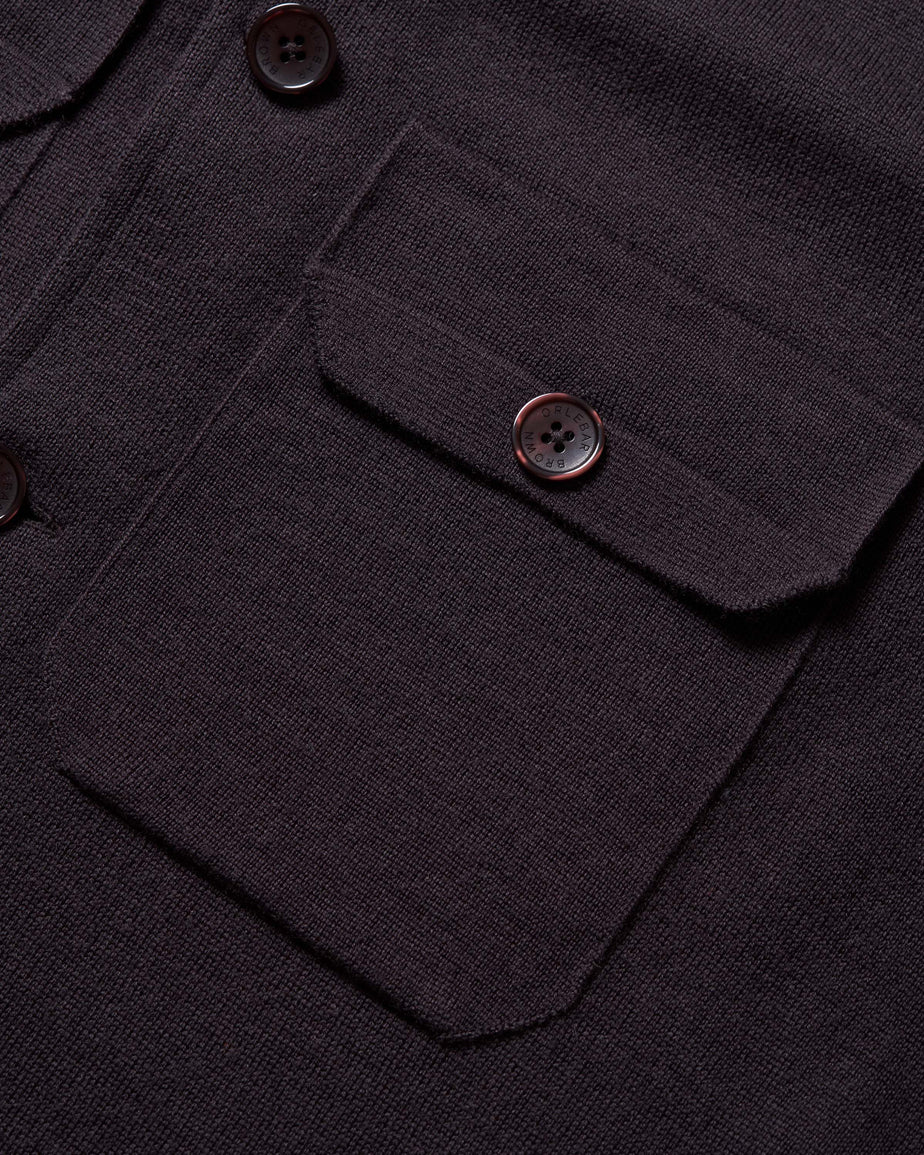 Close-up of a dark charcoal knit button-up shirt showing a chest pocket with a buttoned flap.