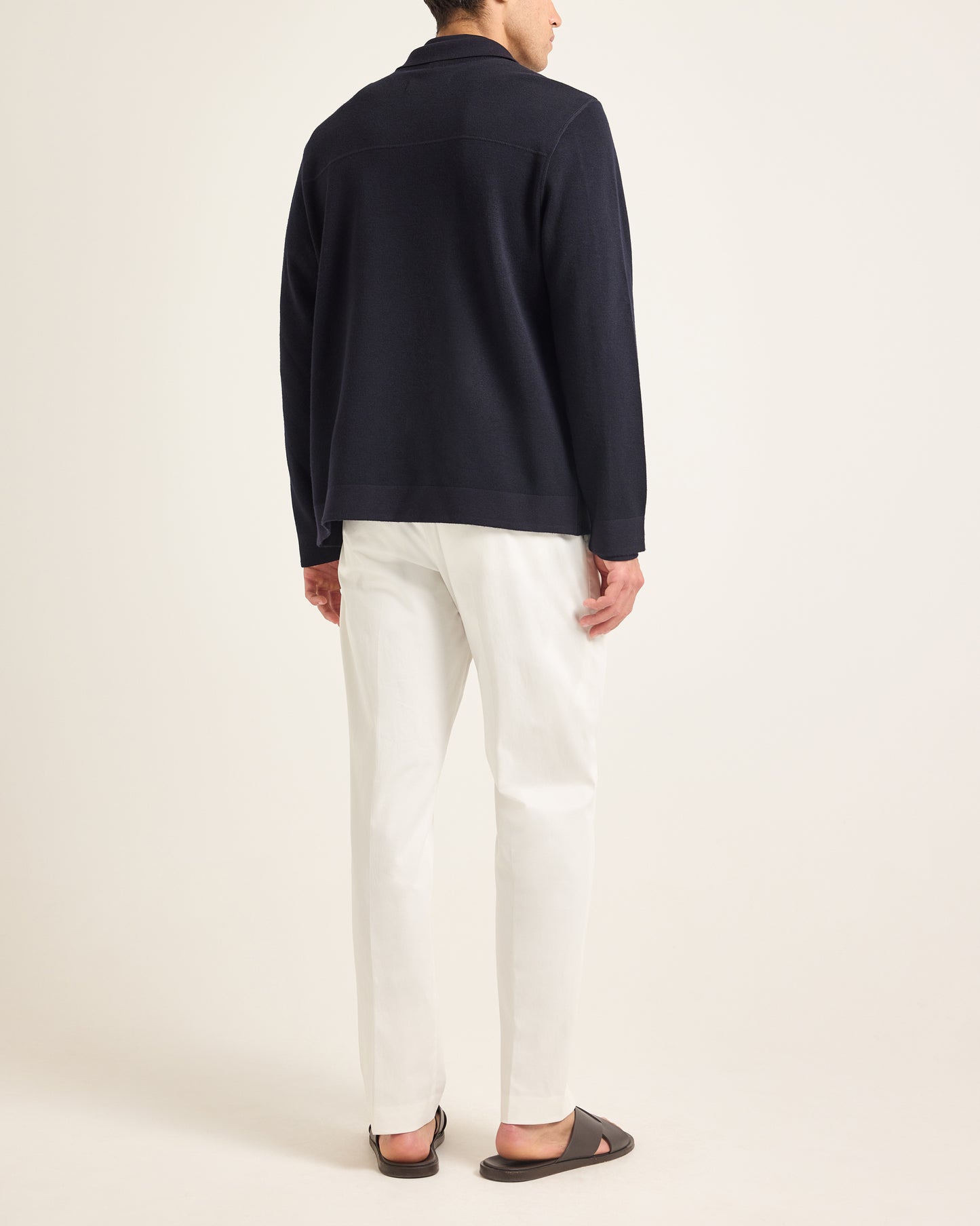 Model wearing navy knitted jacket with navy polo shirt and white trousers on a plain background