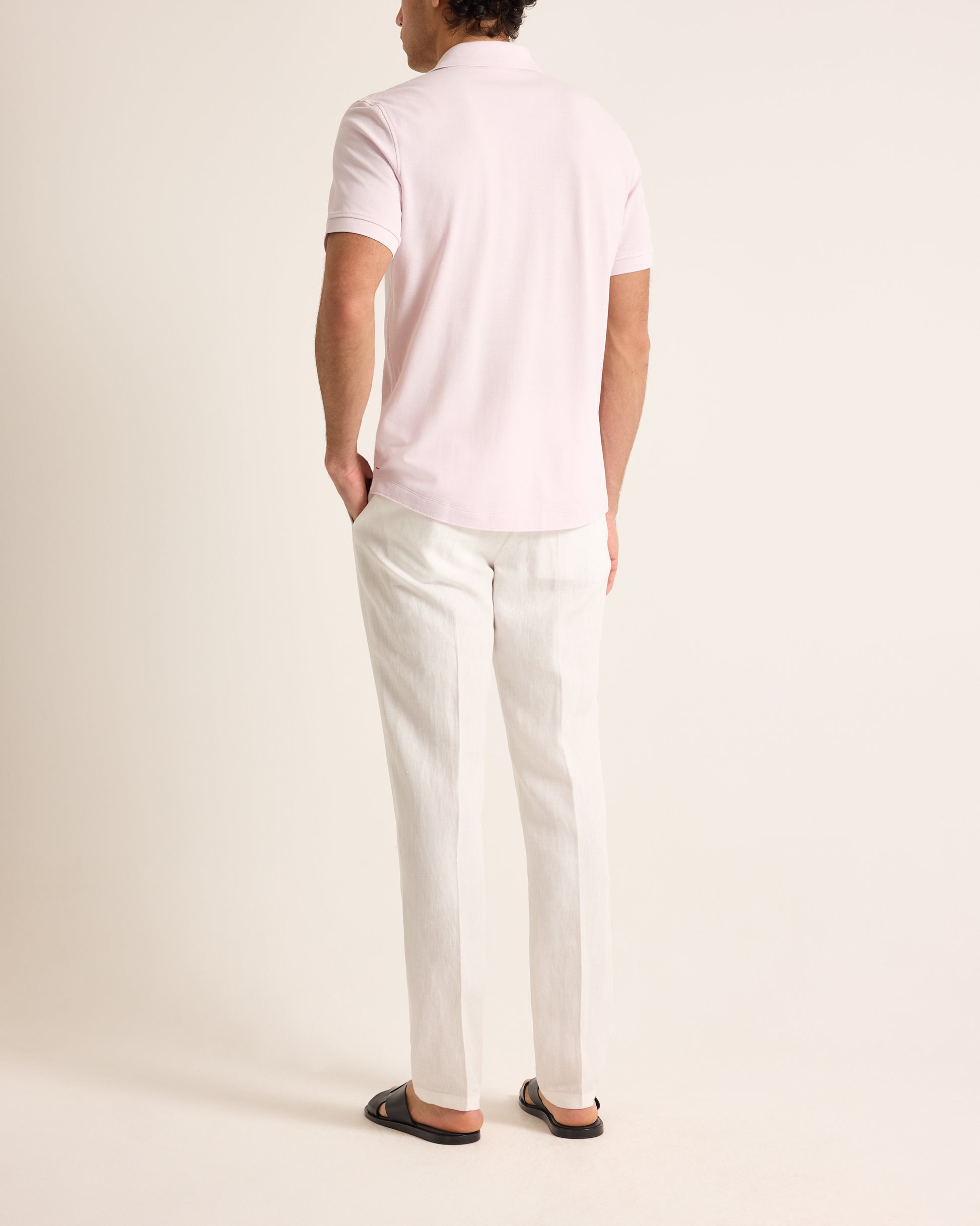 Person wearing a light pink polo shirt and white pants on a plain background