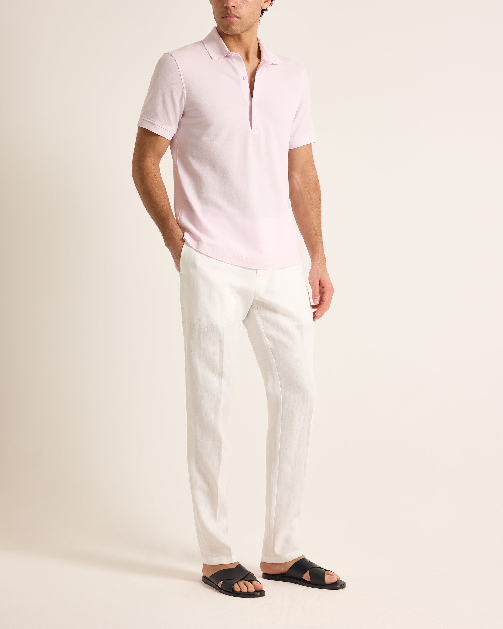 Man wearing a light pink polo shirt and white pants on a plain background
