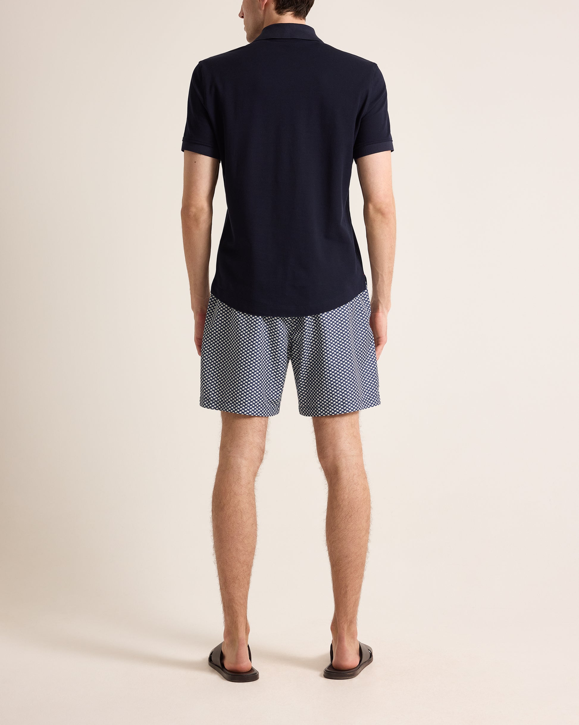 Person wearing a navy polo shirt and patterned shorts on a beige background