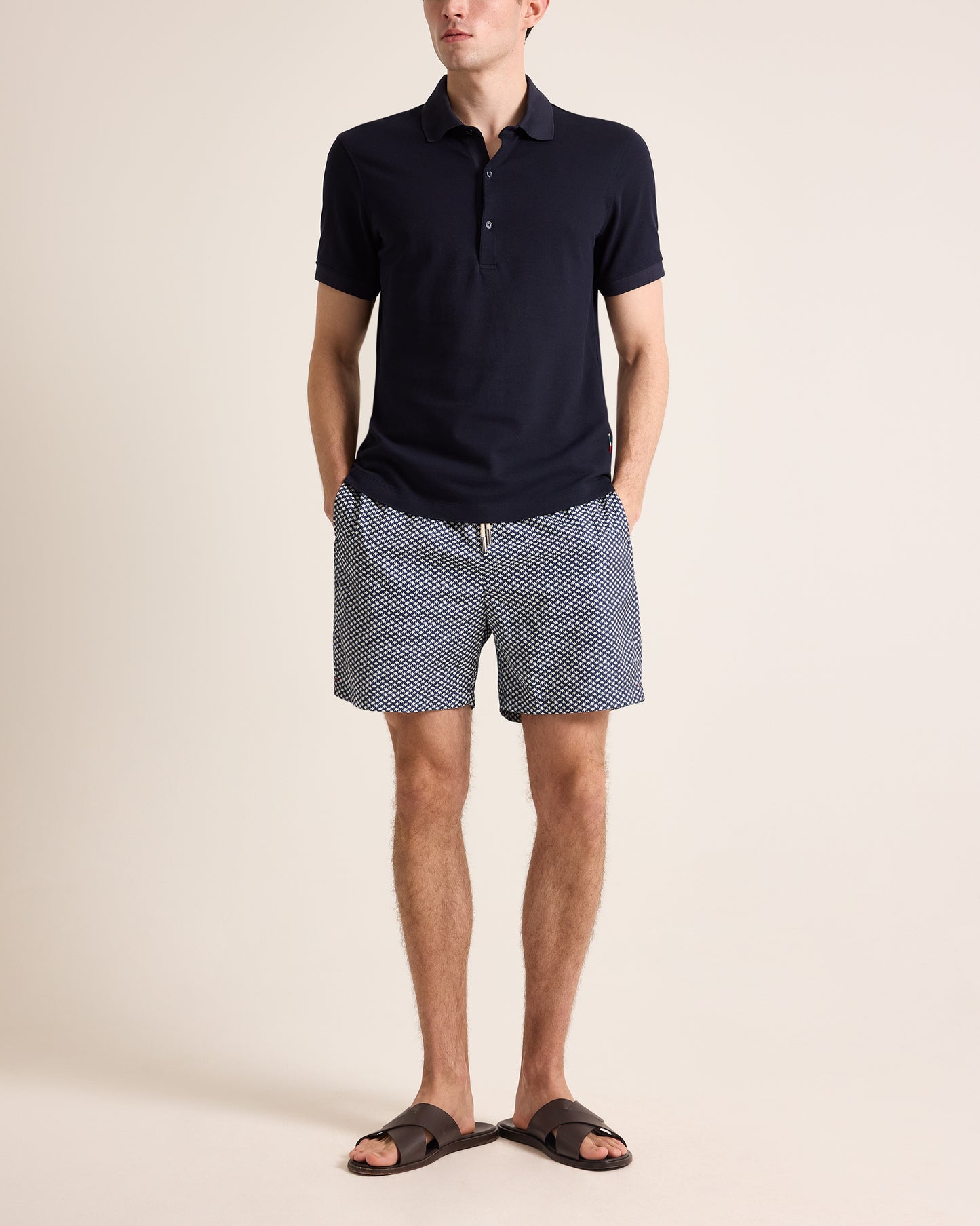 Man wearing a navy polo shirt and patterned shorts on a beige background