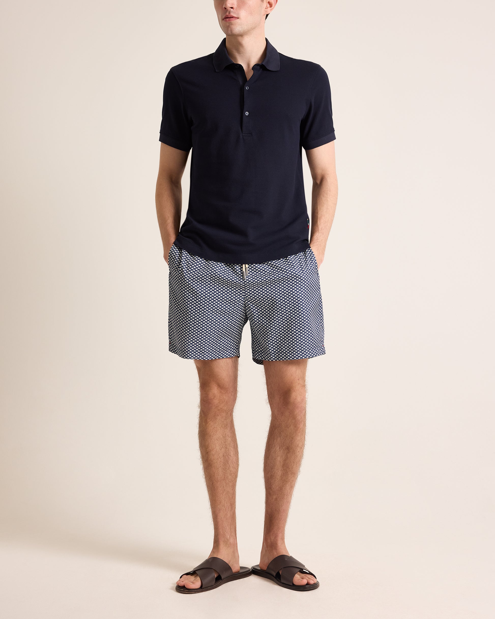Man wearing a navy polo shirt and patterned shorts on a beige background