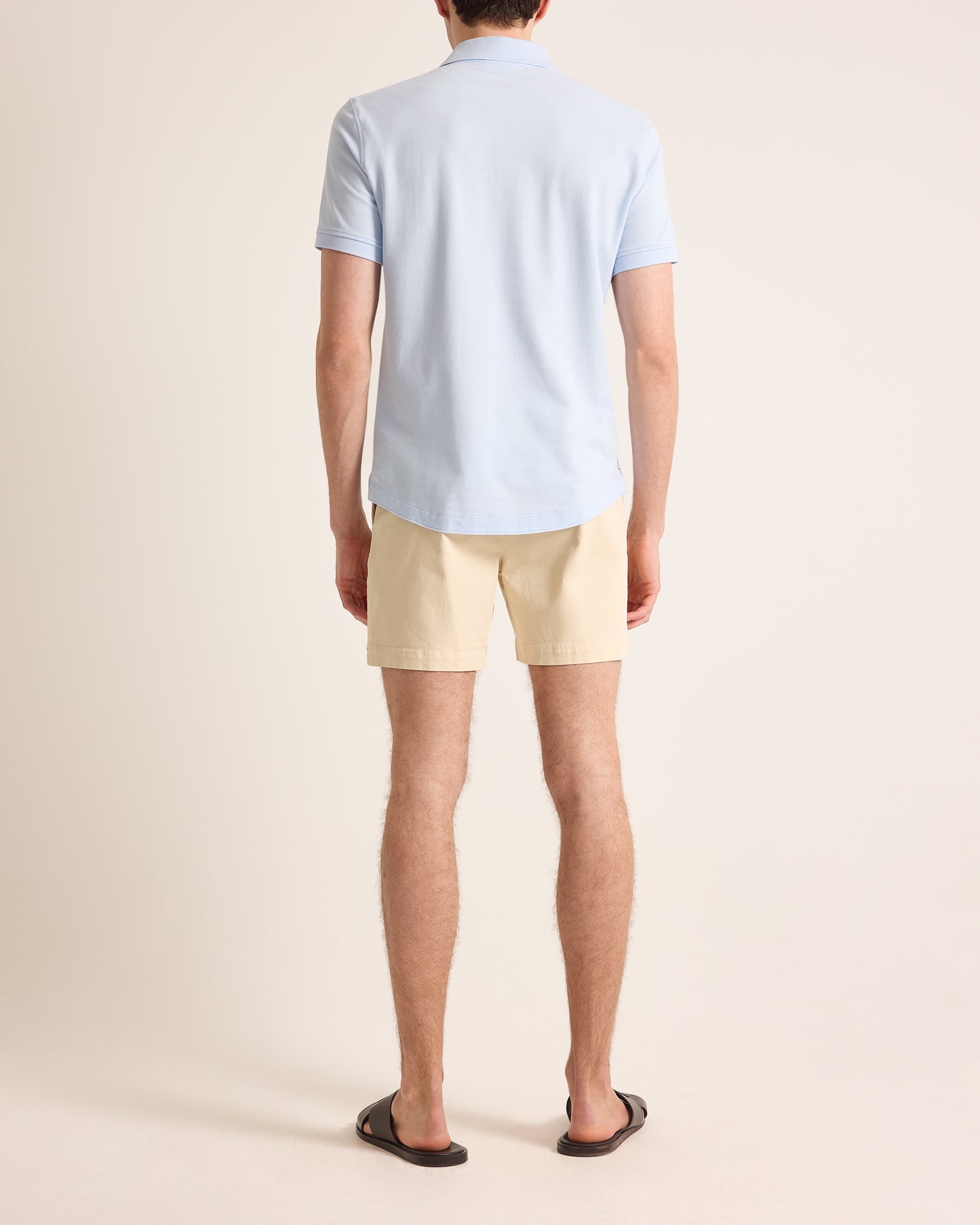 Man wearing light blue polo shirt and beige shorts on a plain background