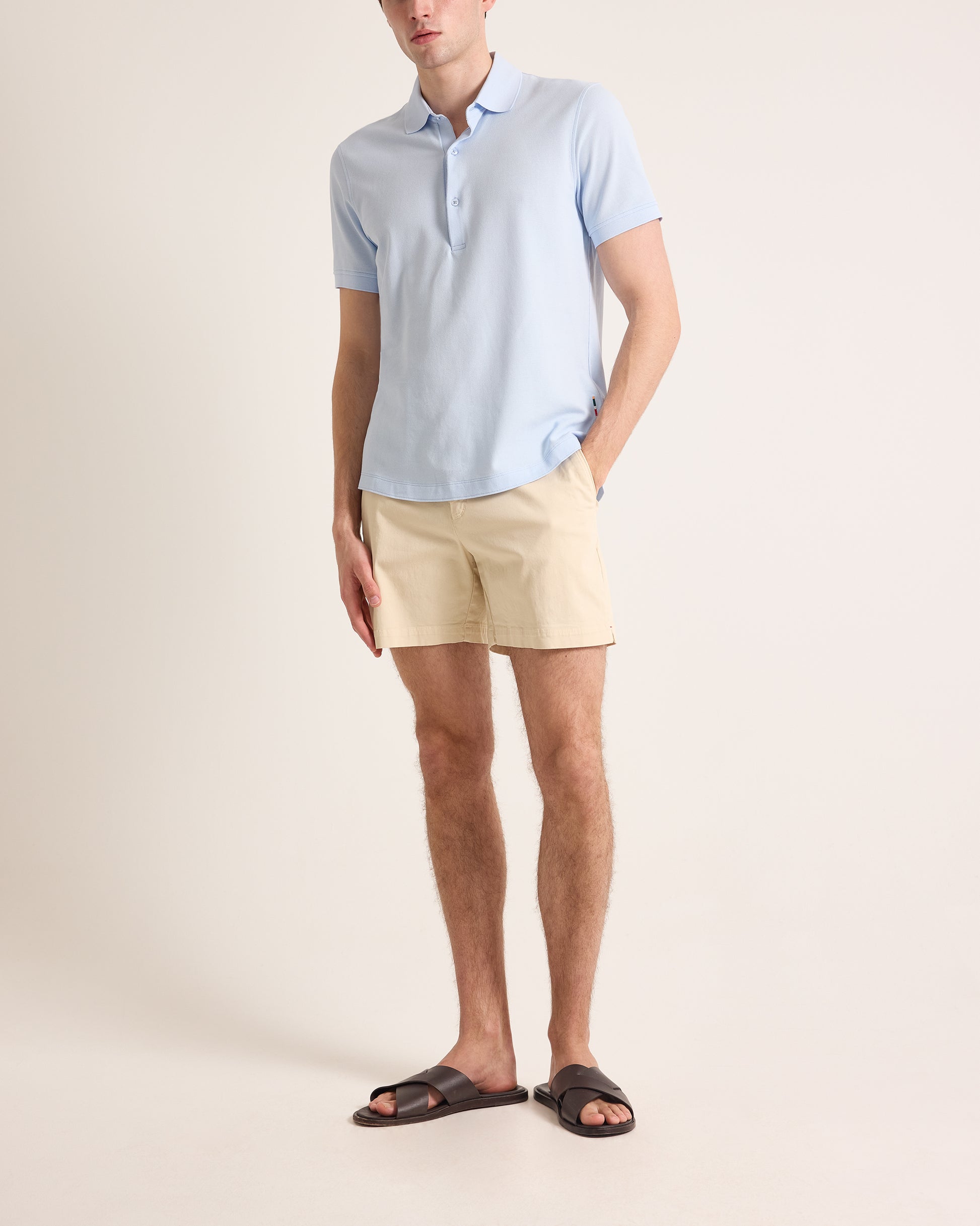Man wearing a light blue polo shirt and beige shorts on a plain background
