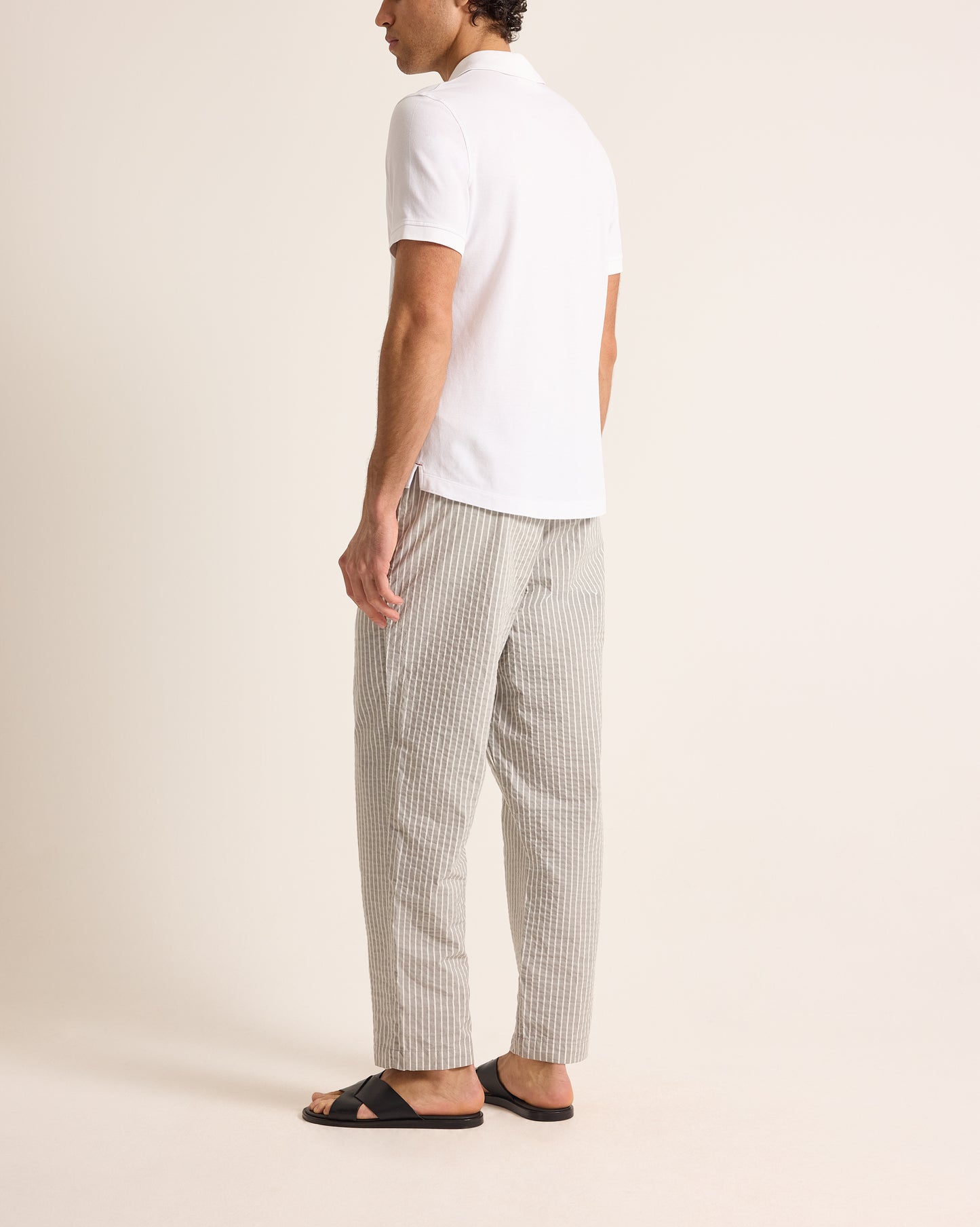 Person wearing a white polo shirt and striped pants on a beige background