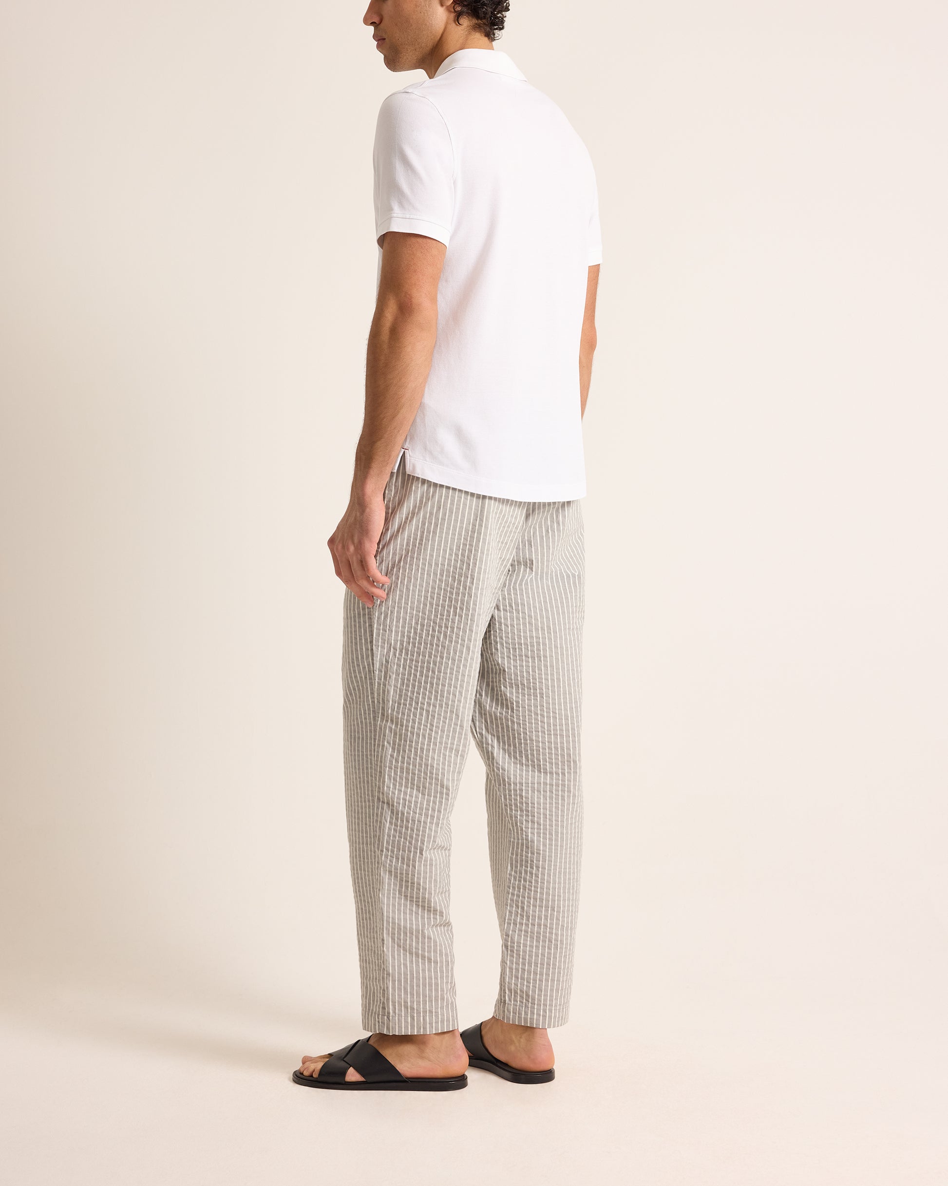 Person wearing a white polo shirt and striped pants on a beige background