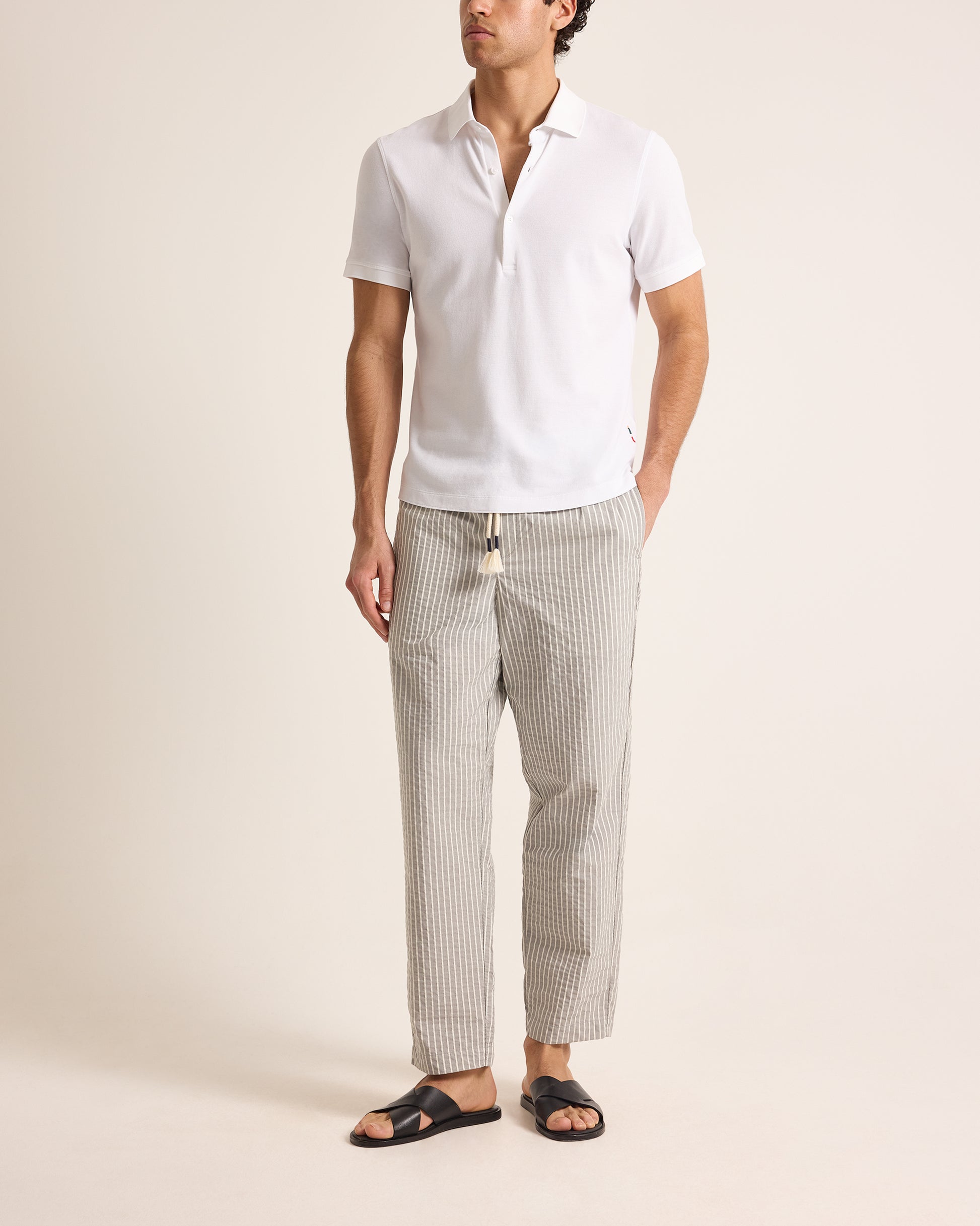 Man wearing a white polo shirt and striped pants on a beige background
