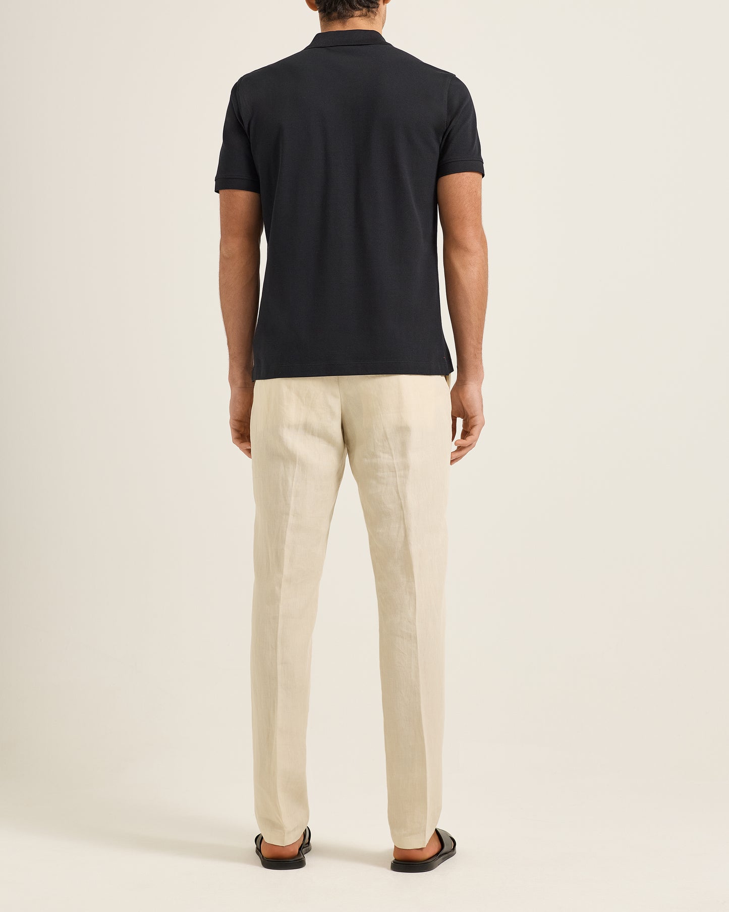 Person wearing a black polo shirt and beige pants on a plain background