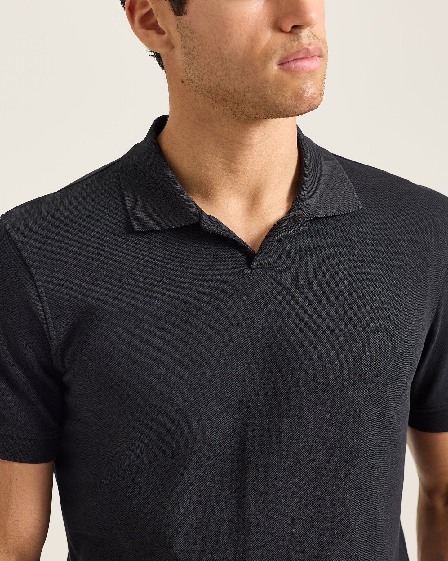 Man wearing a black polo shirt against a neutral background