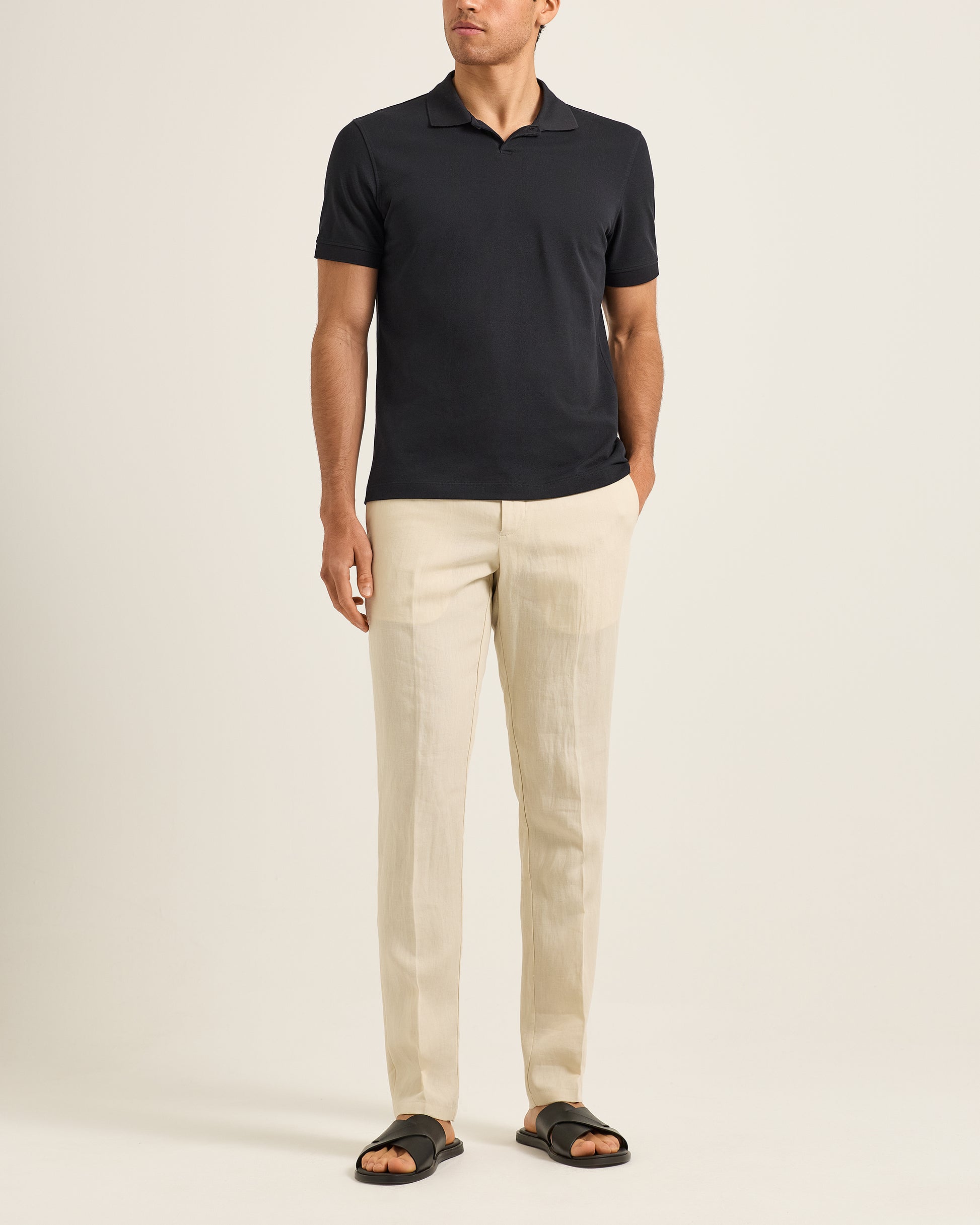 Man wearing a black polo shirt and beige pants on a white background
