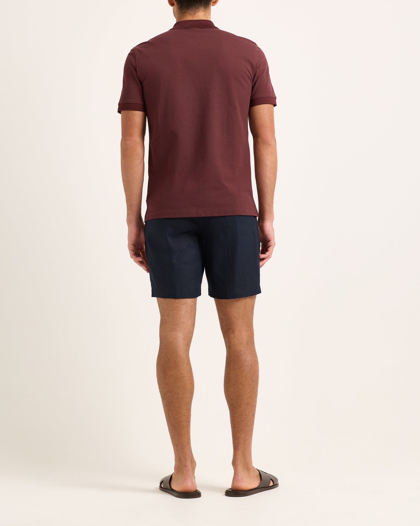 Model wearing dark red polo with navy shorts on a white backgruound