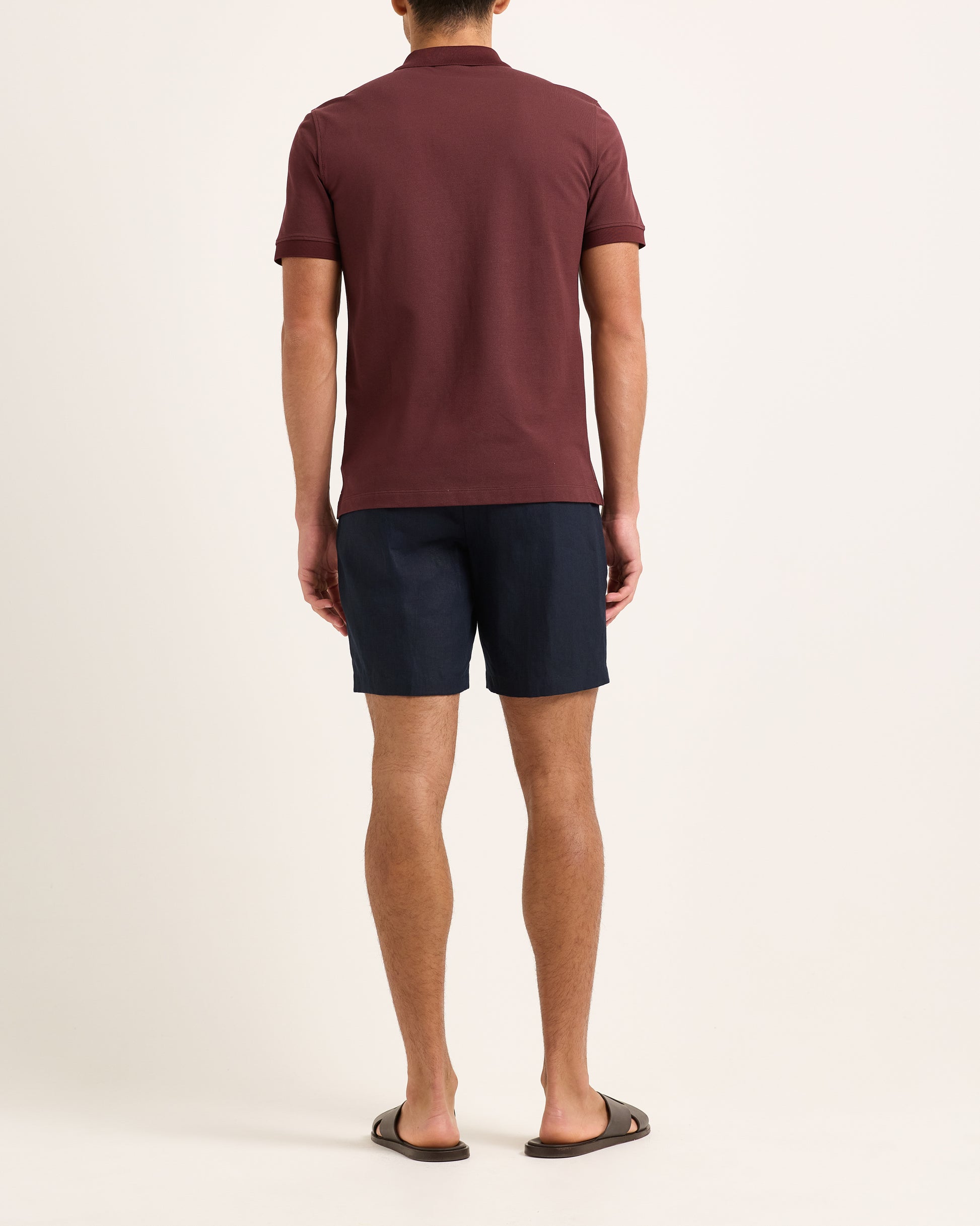 Model wearing dark red polo with navy shorts on a white backgruound