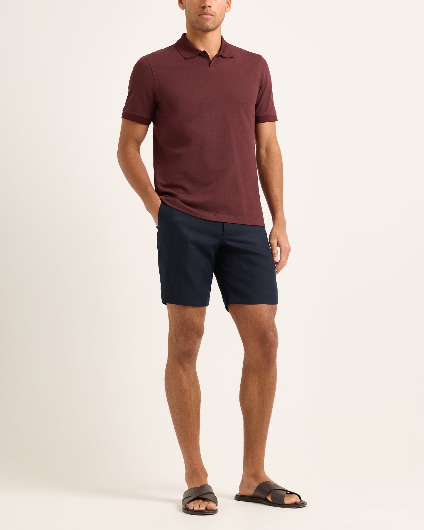 Man wearing a maroon polo shirt and navy shorts on a white background