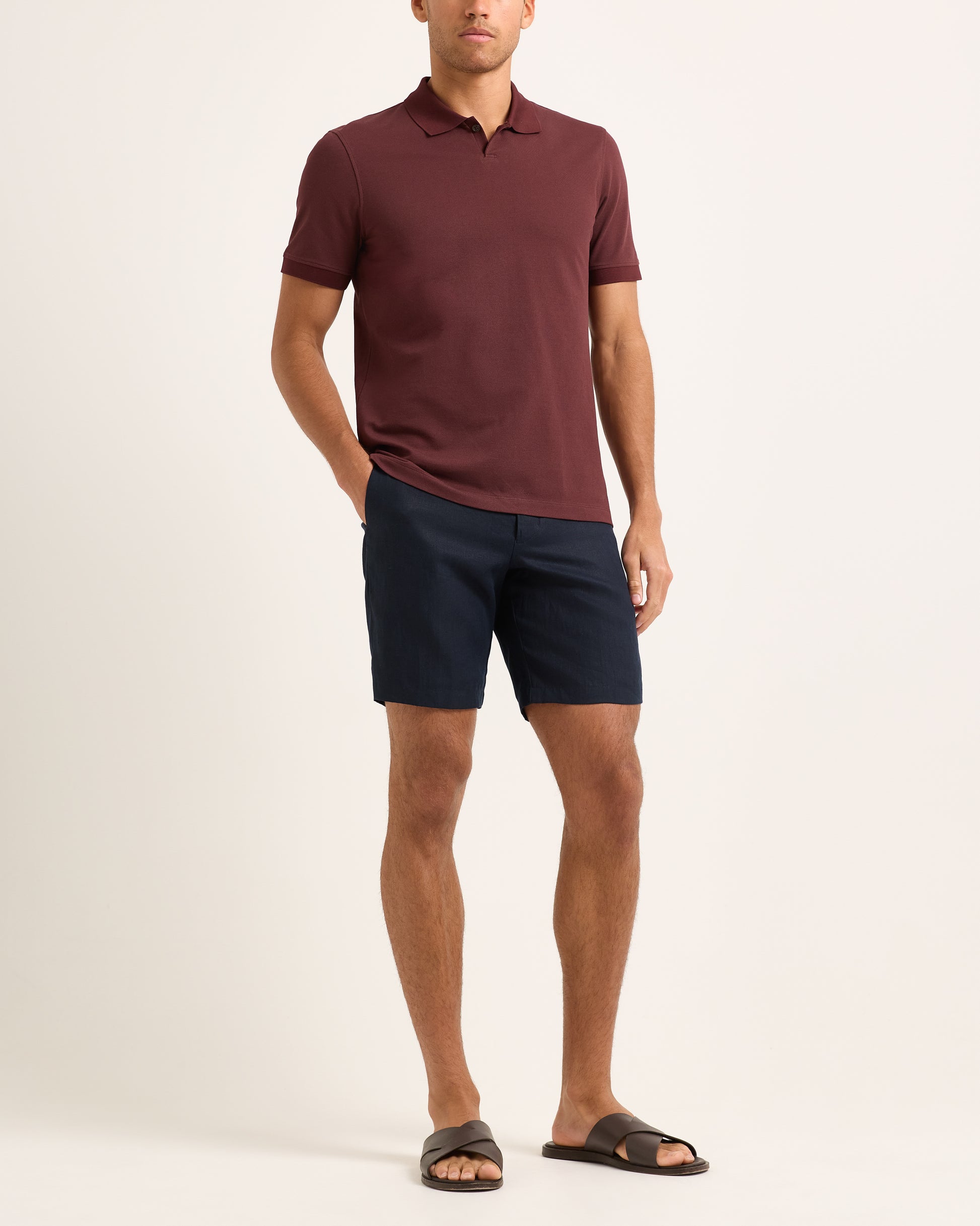 Man wearing a maroon polo shirt and navy shorts on a white background