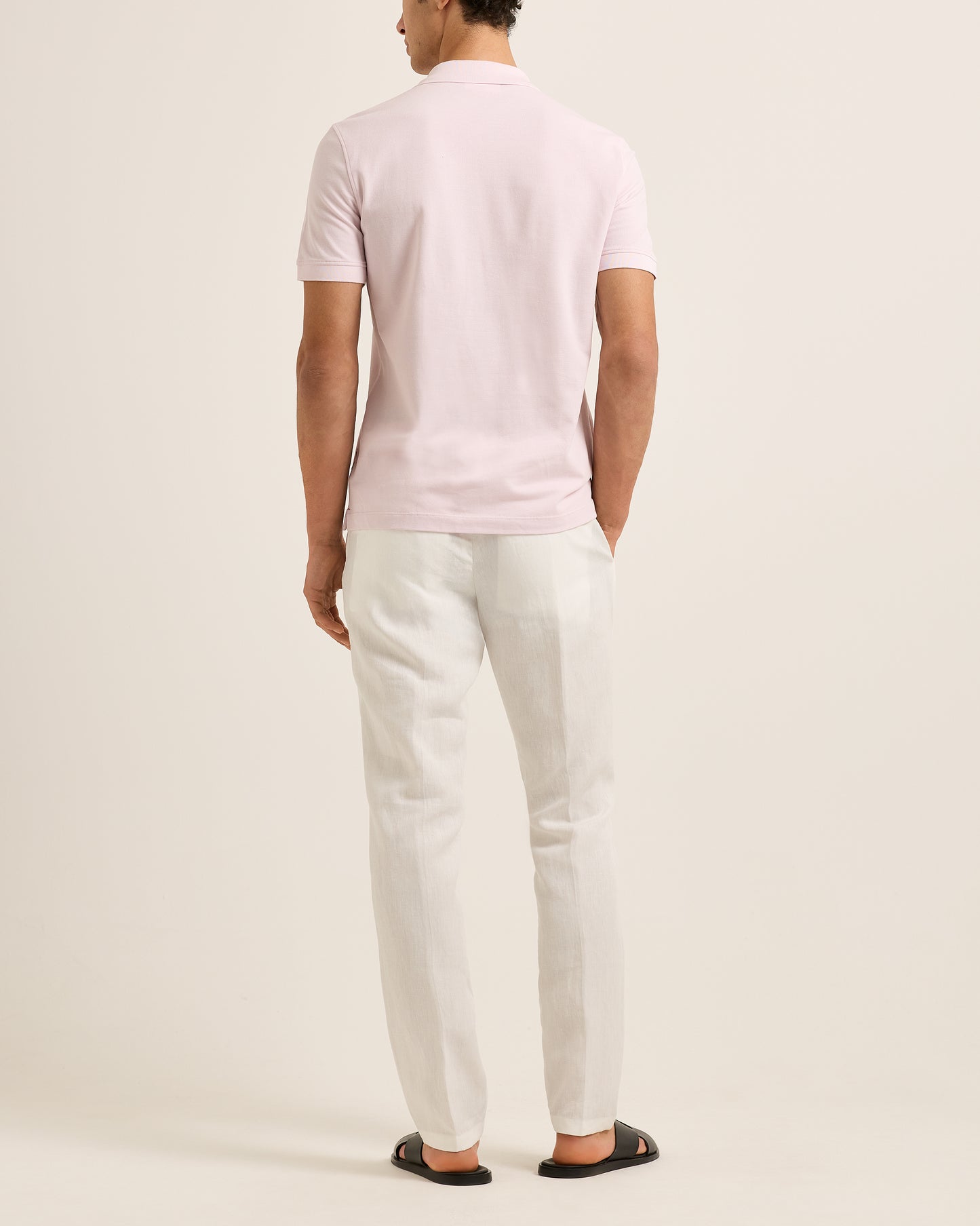 Person wearing a light pinkpolo shirt and white pants on a plain background