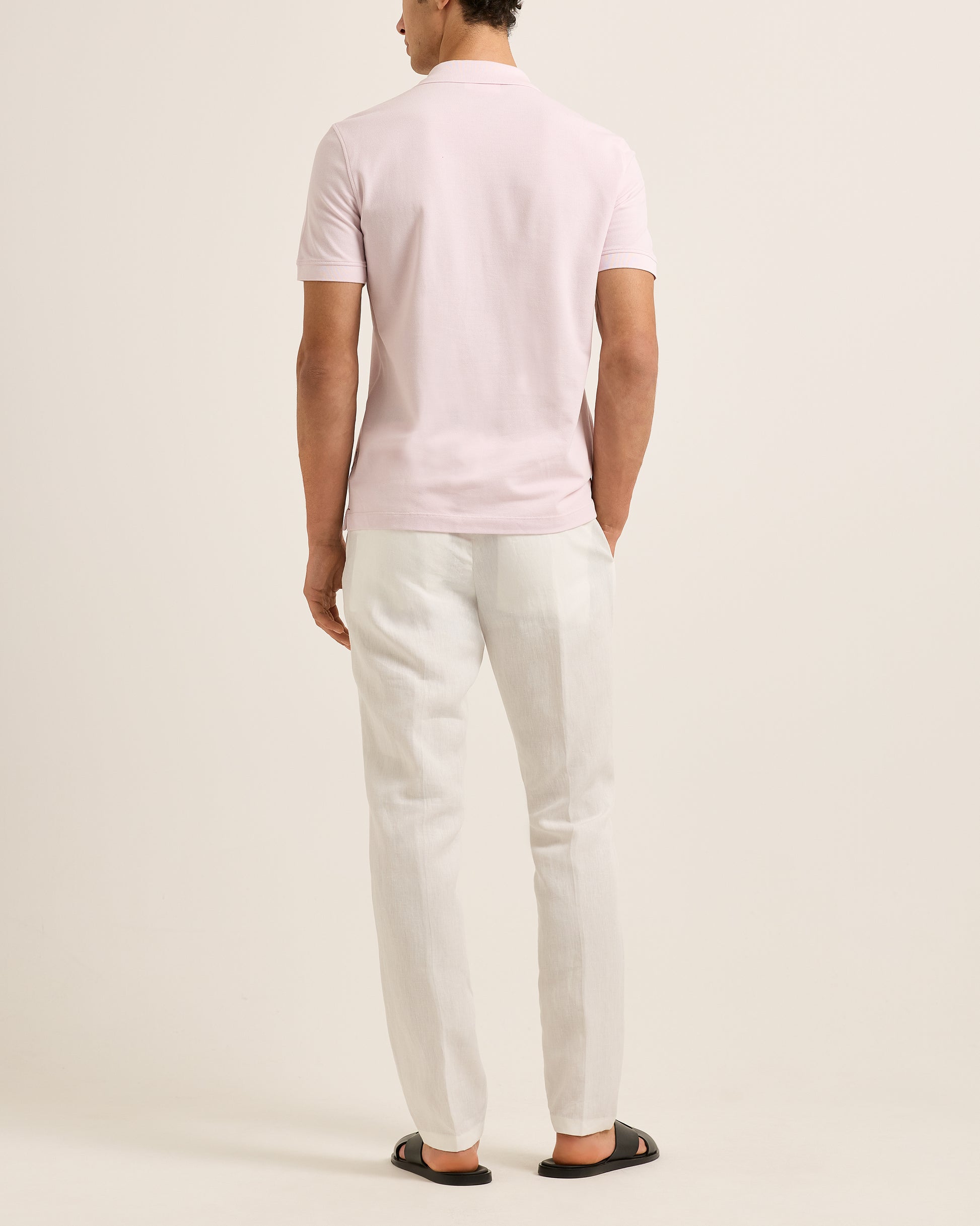 Person wearing a light pinkpolo shirt and white pants on a plain background
