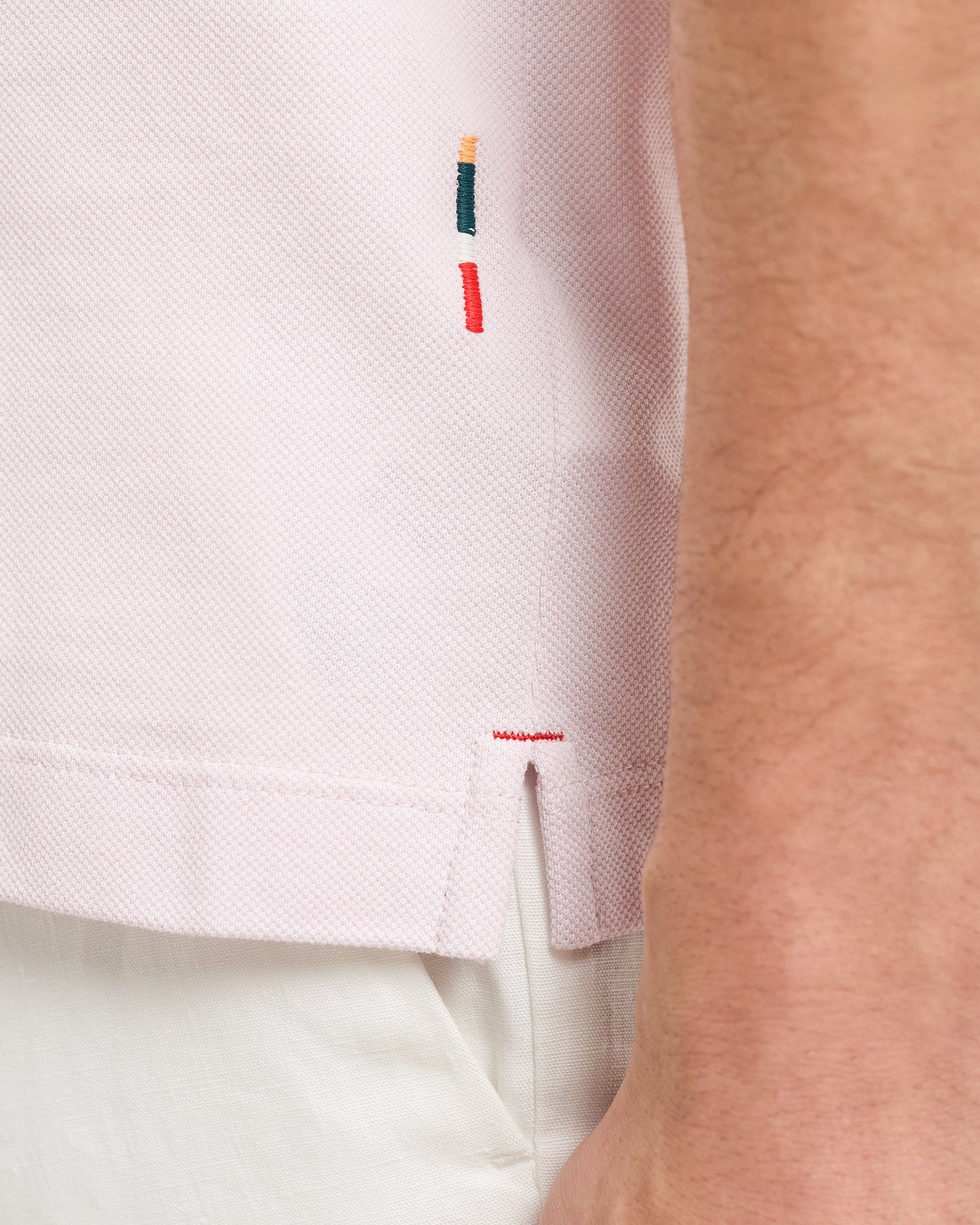 Close-up of a light pink shirt with embroidered details on a person wearing it.