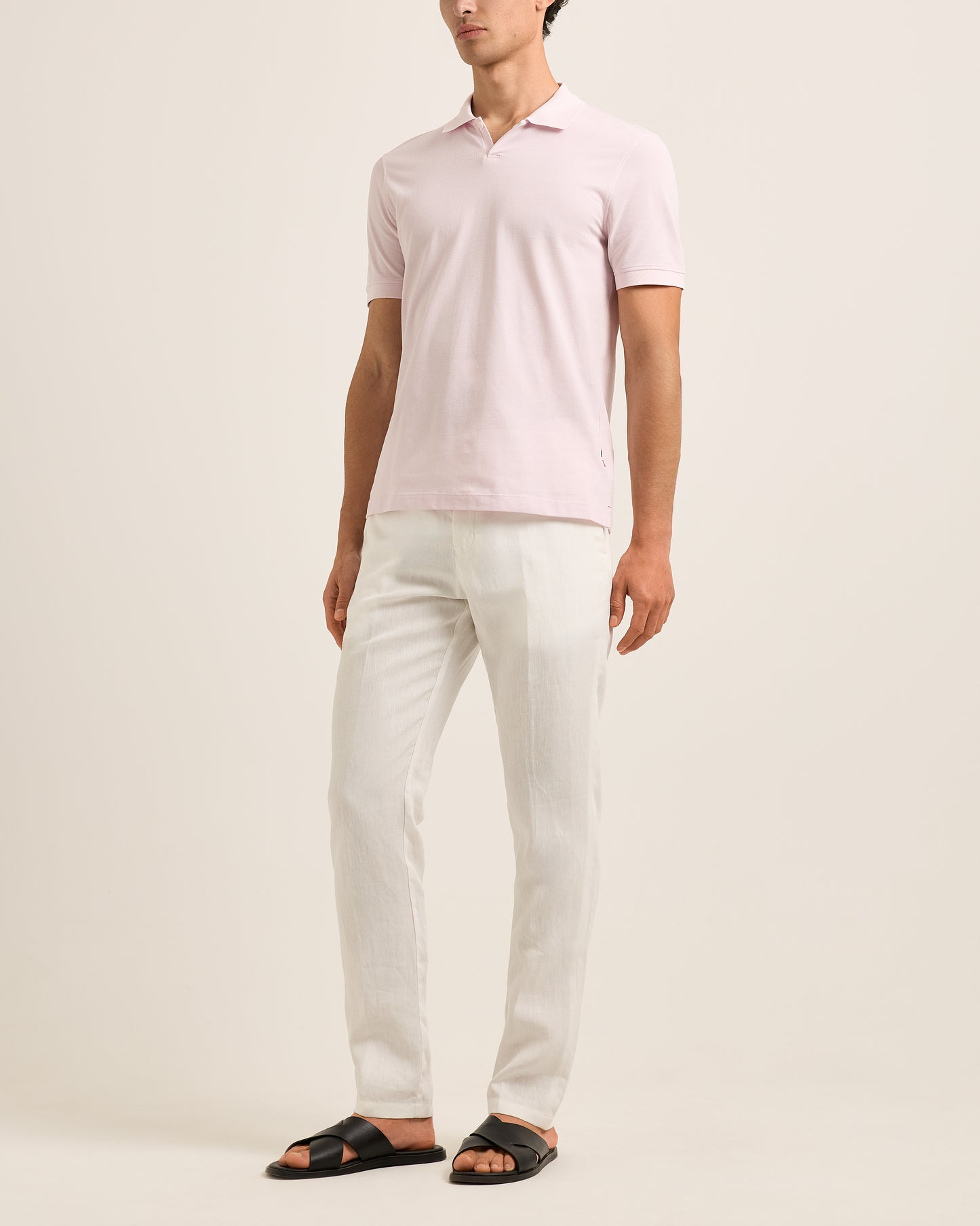 Person wearing a light pink polo shirt and white pants on a beige background