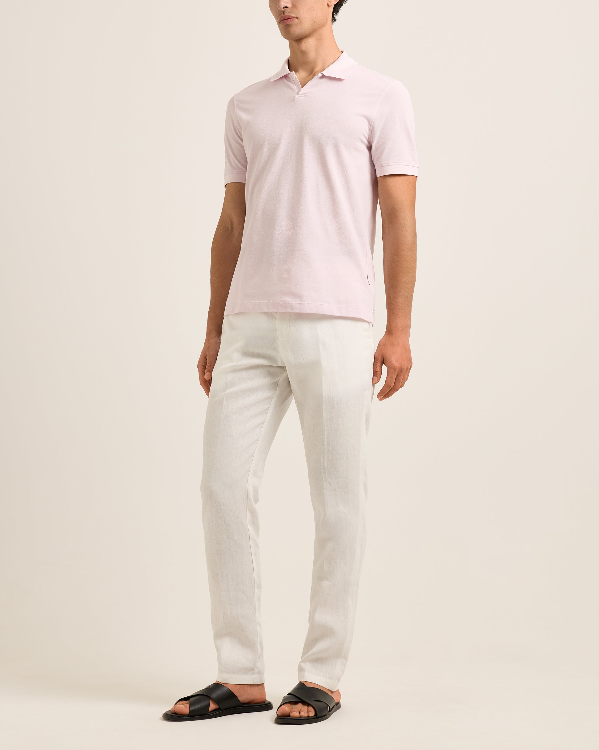 Person wearing a light pink polo shirt and white pants on a beige background