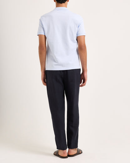 Man wearing a light blue polo shirt and dark pants on a white background