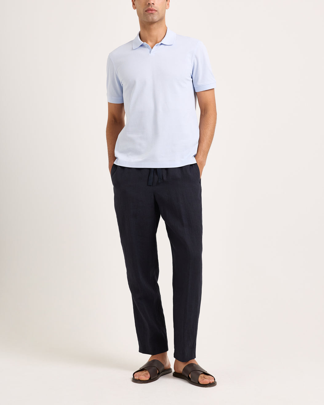 Man wearing a light blue polo shirt and dark pants on a white background