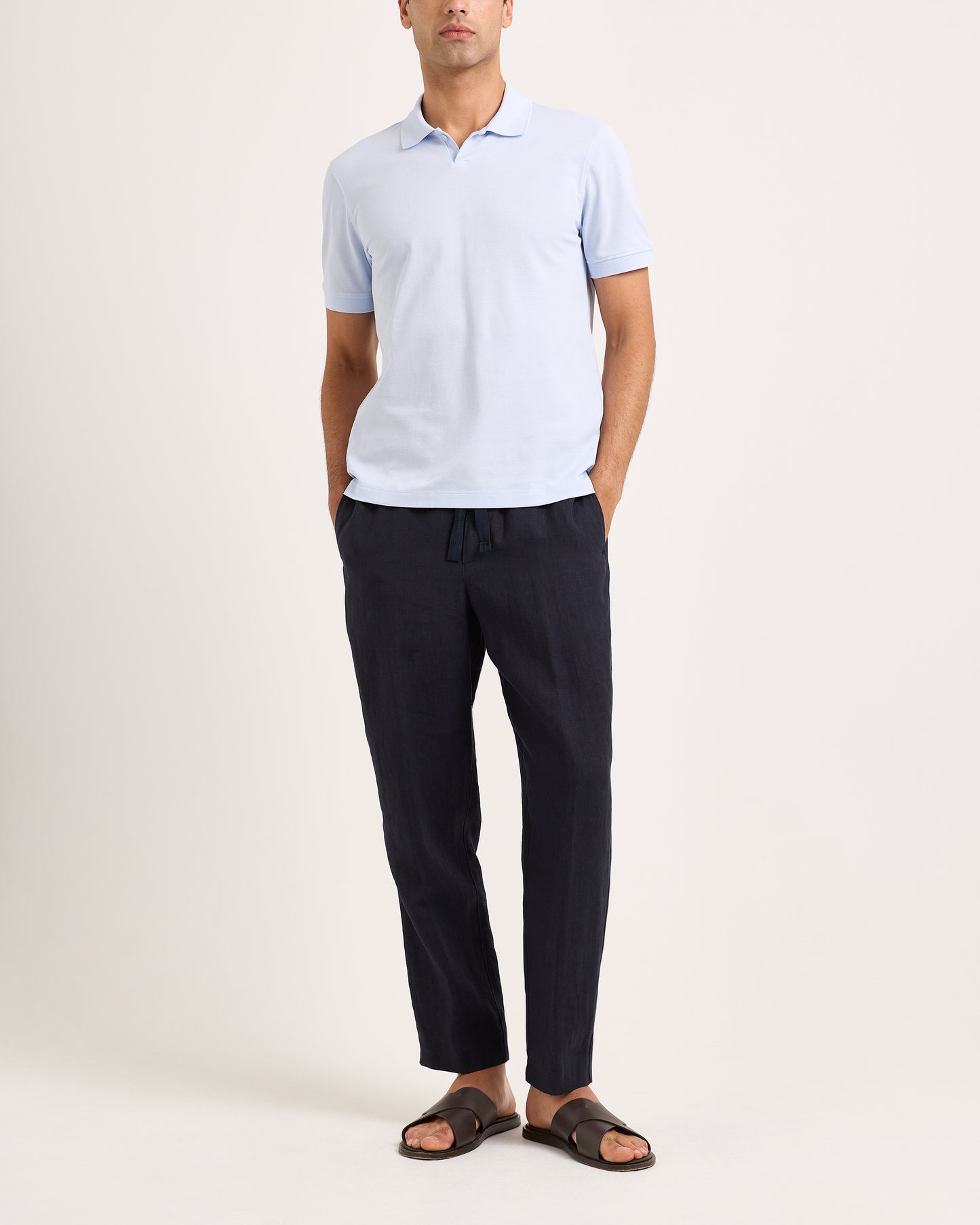 Man wearing a light blue polo shirt and dark pants on a white background