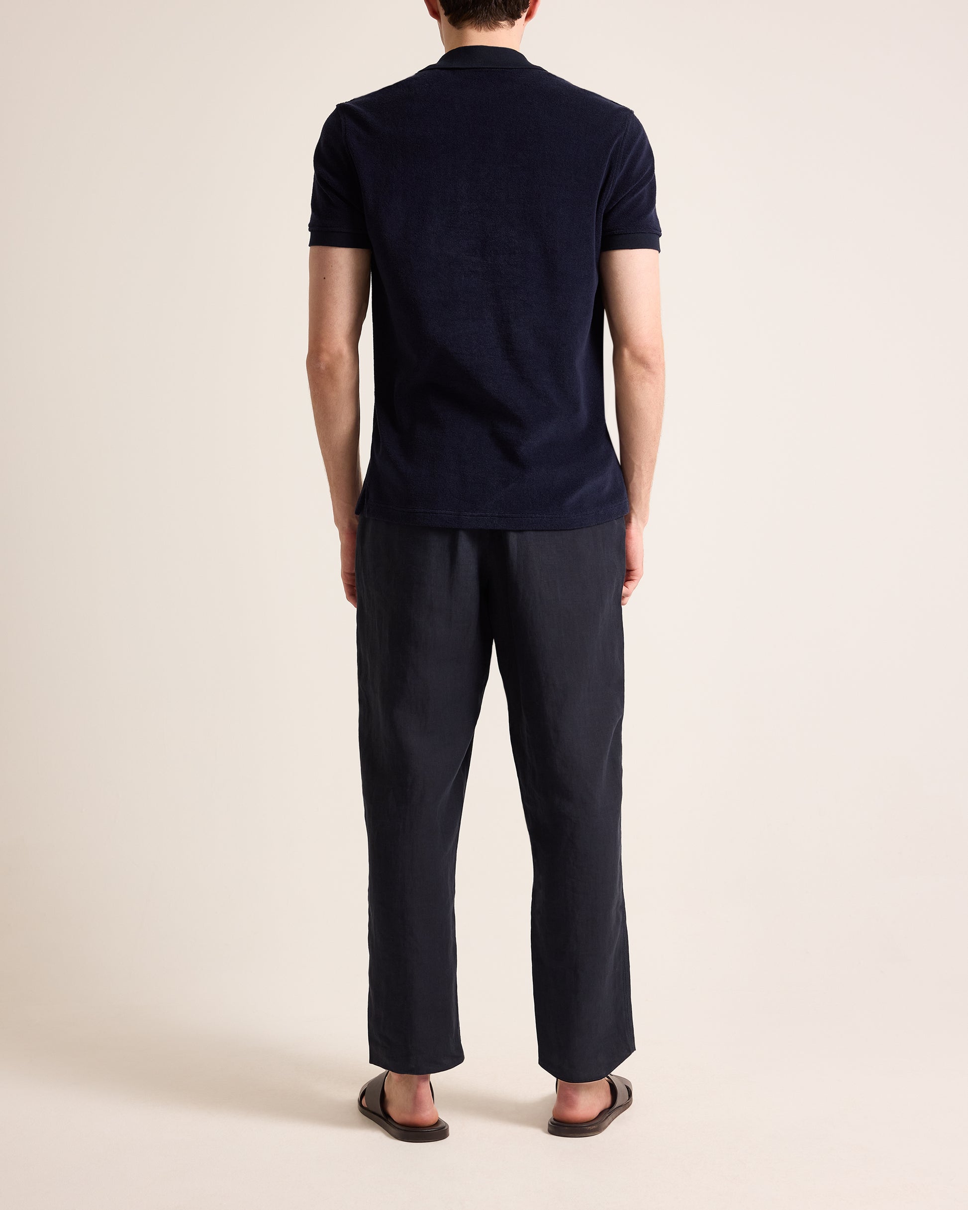 Person wearing navy towelling polo shirt and navy linen trousers on a plain background