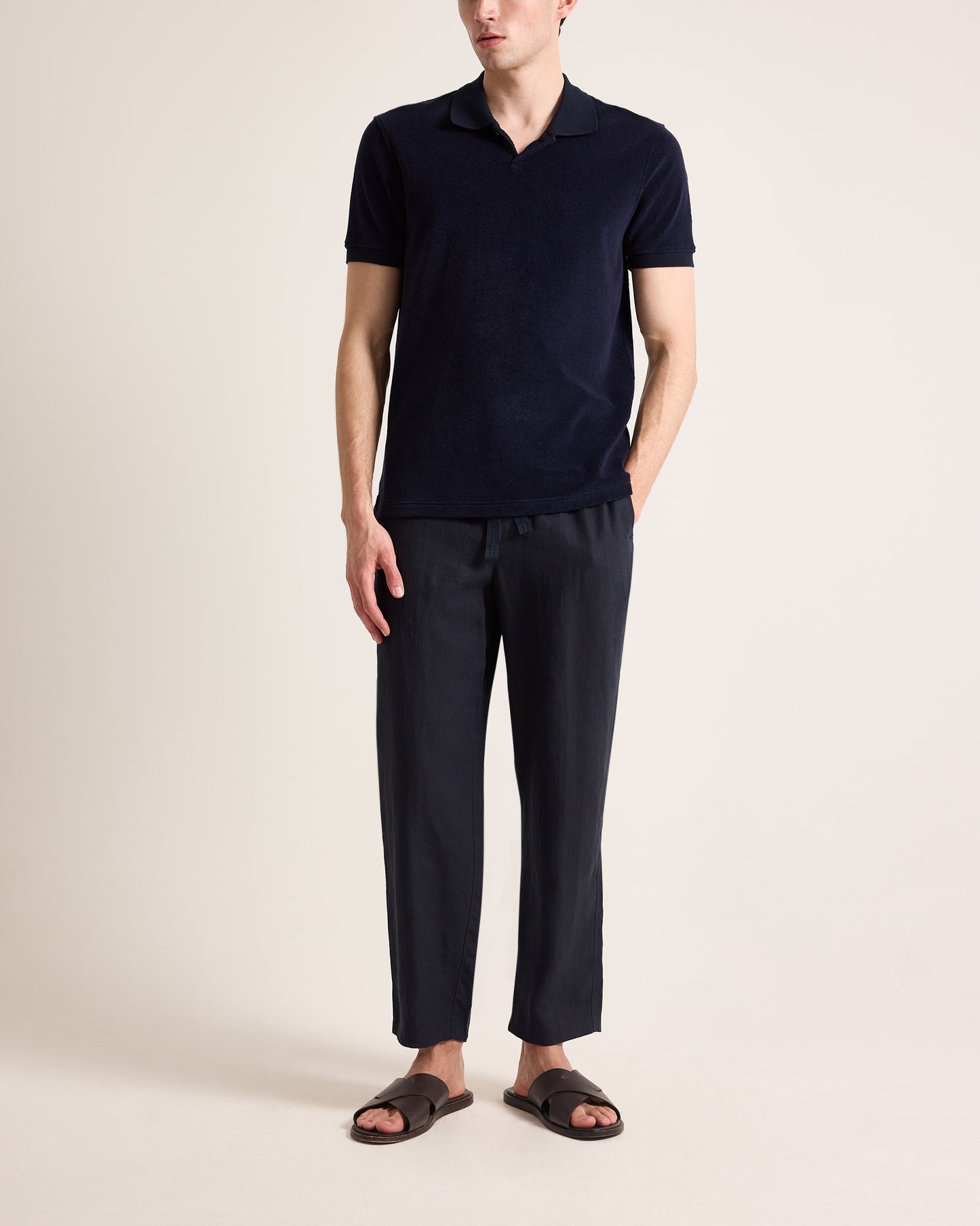 Person wearing navy towelling polo shirt and navy linen trousers on a plain background