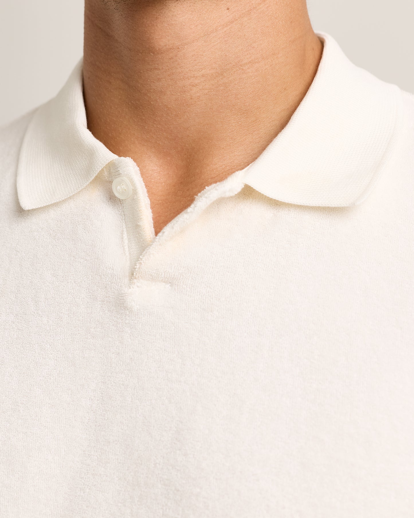 Close up detail of collar, model is wearing light cream towelling polo on white background