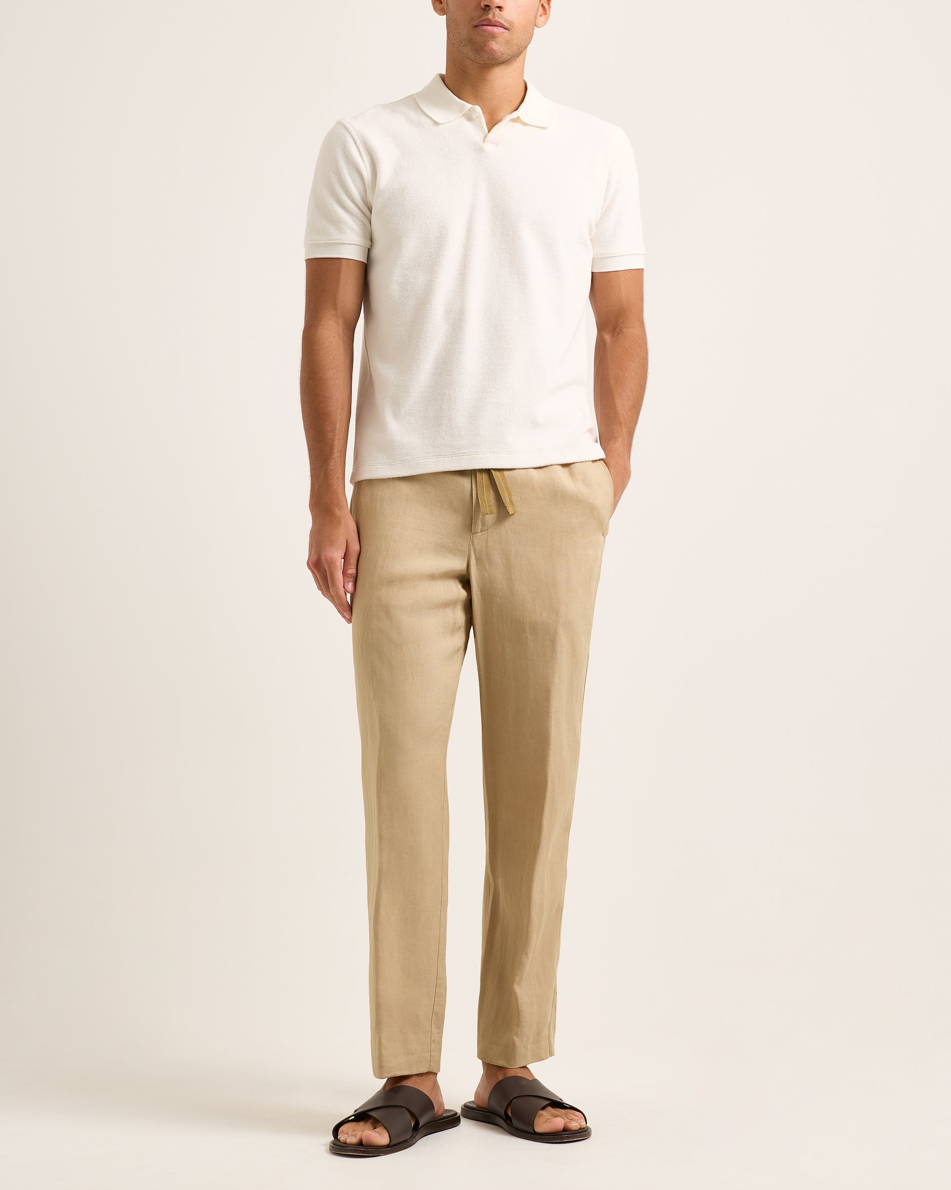 Man wearing a white polo shirt and beige pants on a plain background